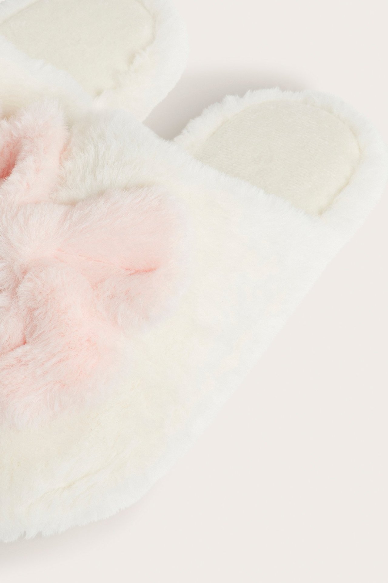 Lähikuva luonnonvalkoisesta tekoturvistohvelista, jossa on vaaleanpunainen tekoturkisrusetti.