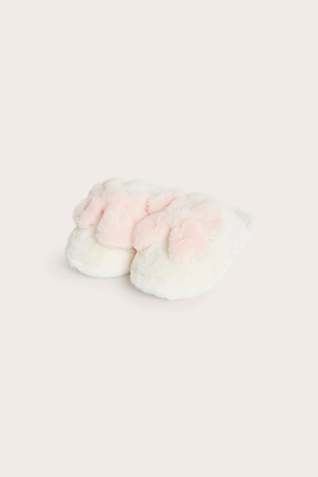 Lähikuva luonnonvalkoisista tekoturkisslippereistä, joissa on vaaleanpunaiset rusetit päällä.