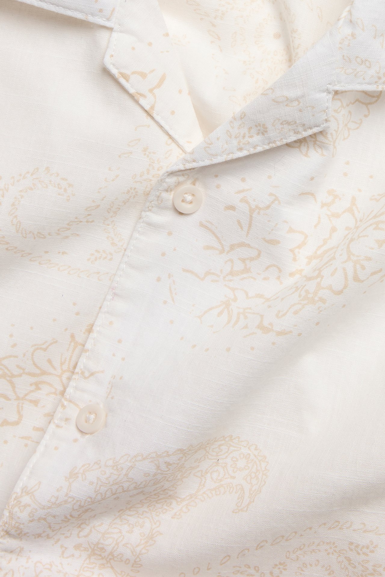 Zbliżenie na kremową, bawełnianą koszulę z krótkim rękawem, beżowym wzorem paisley i kołnierzem resortowym.