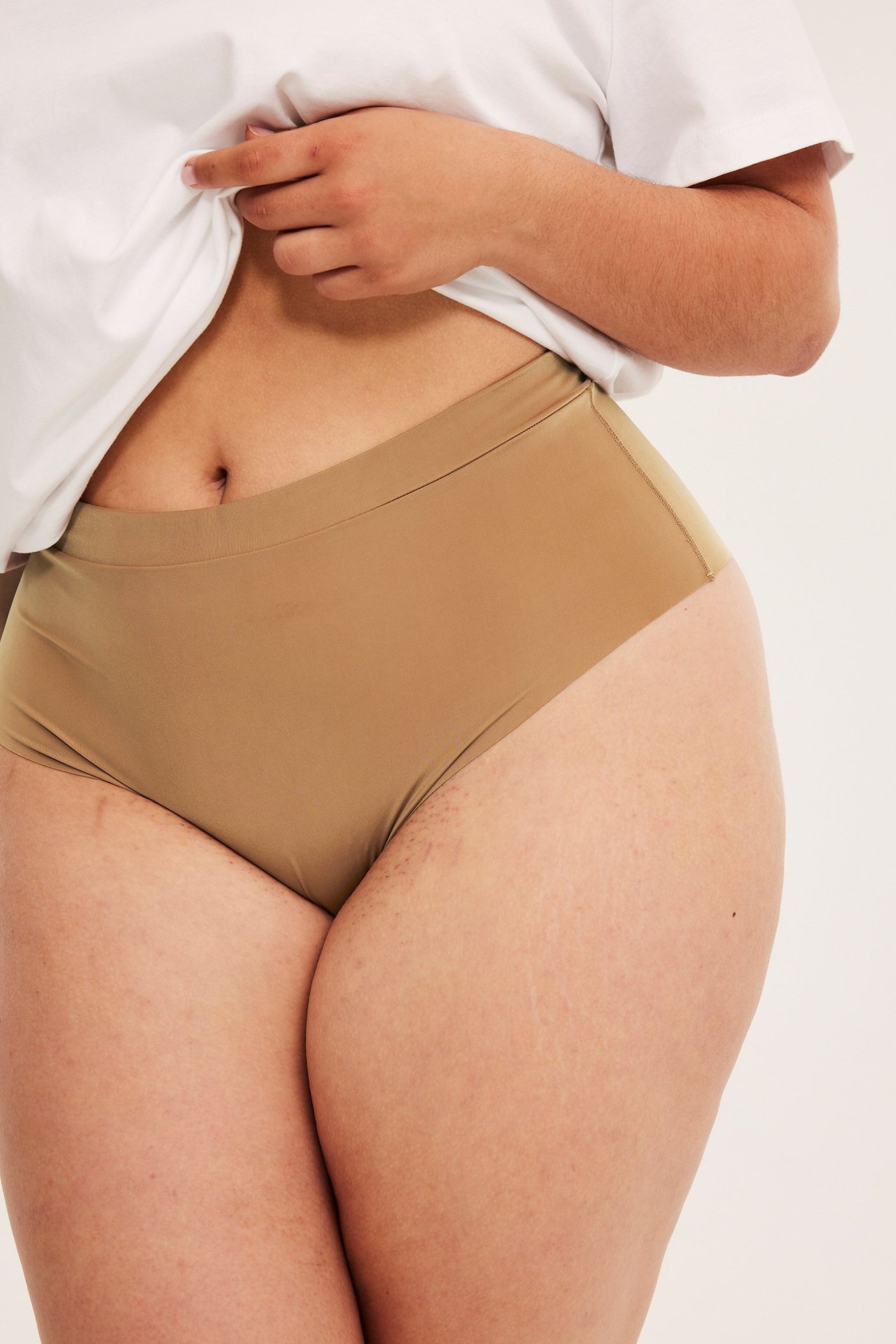 Lähikuva naisesta ruskeissa saumattomissa mikrokangas-alushousuissa valkoisen t-paidan alla.