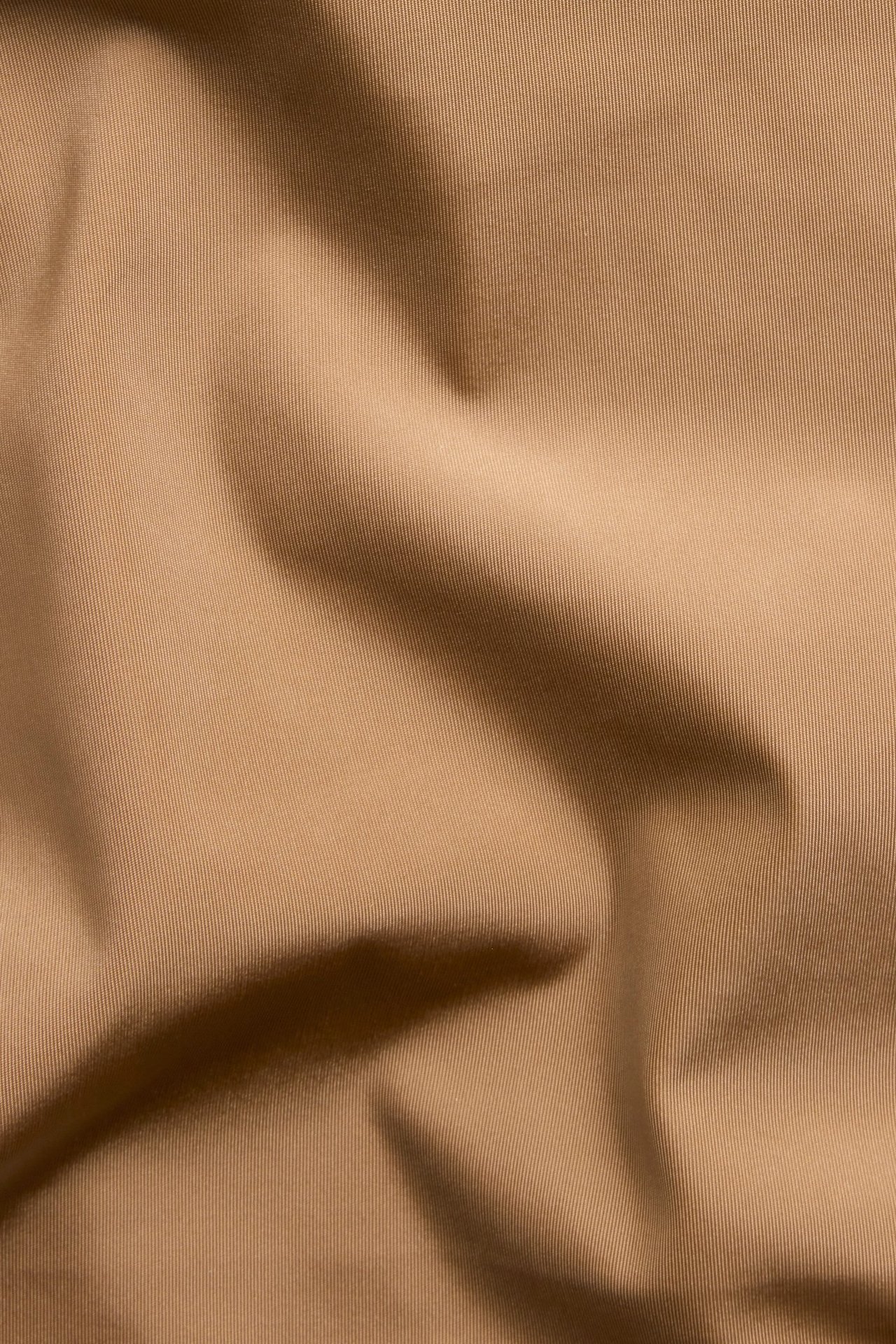 Zbliżenie brązowego, jednolitego materiału mikro z subtelną teksturą i fałdami.