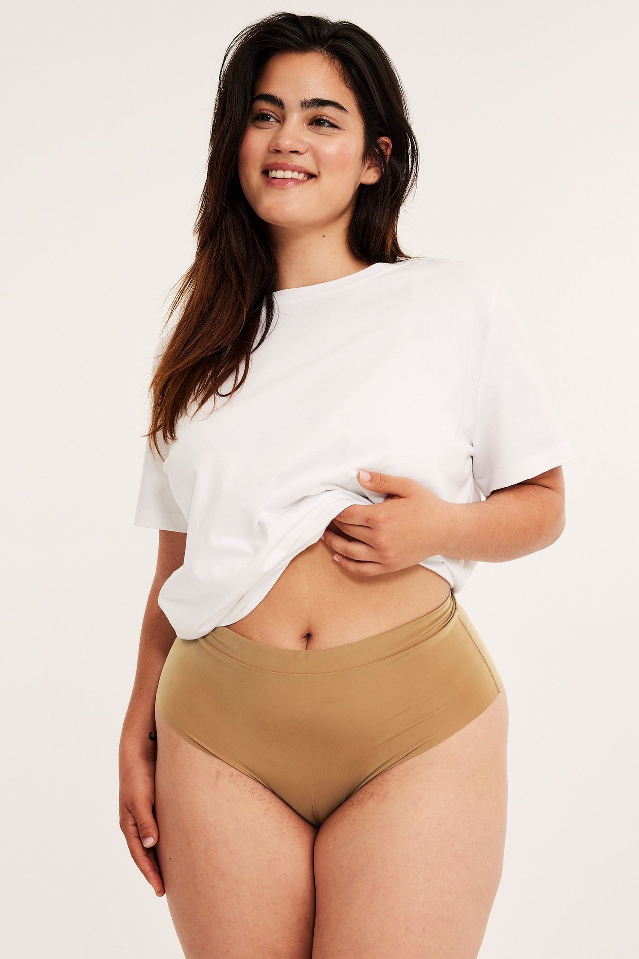 Forfra: kvinne i brune mikro stringtruser med elastisk linning og en hvit t-skjorte.