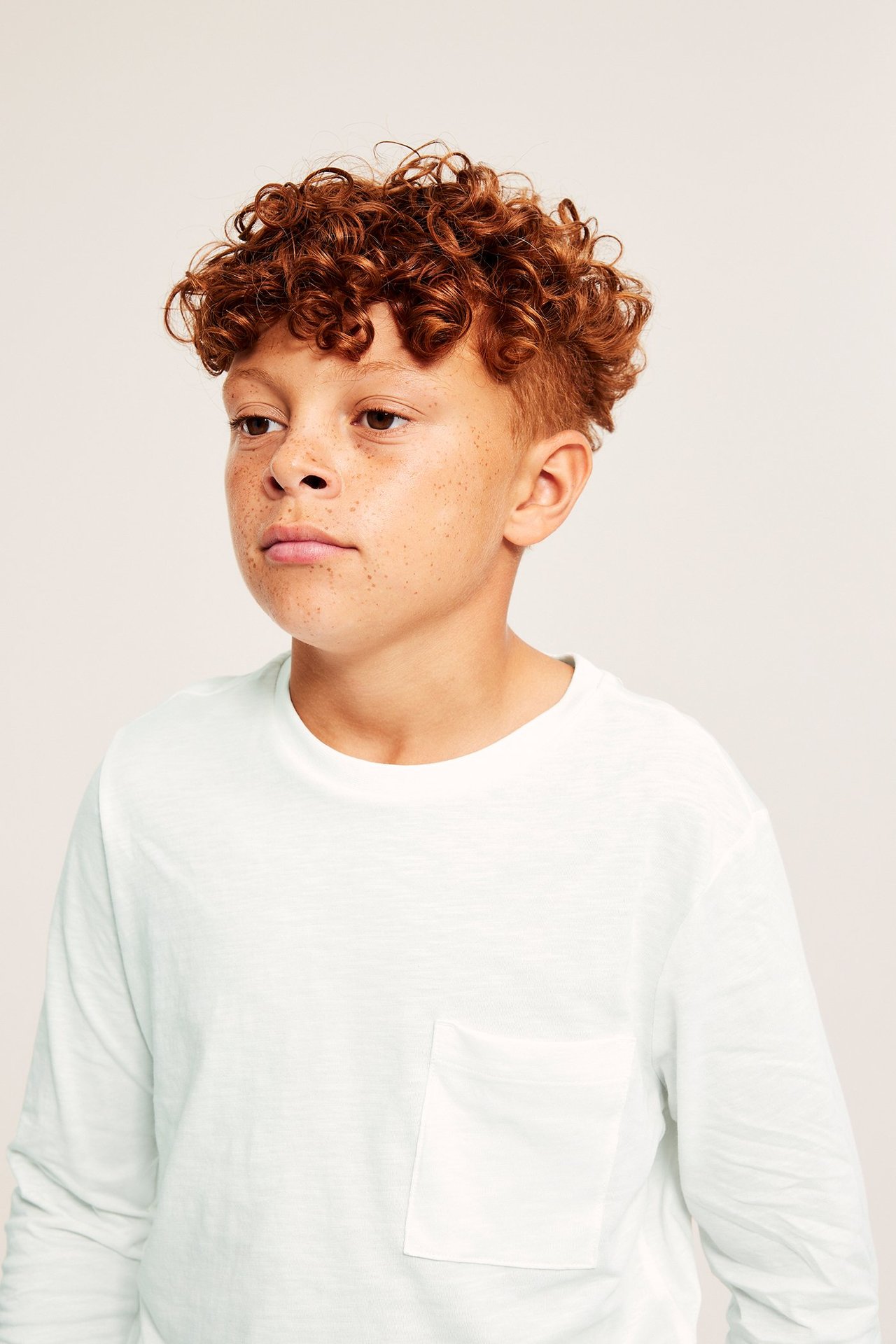 Manlig teenager i vit, långärmad t-shirt med ficka i slubmaterial, frontvy.