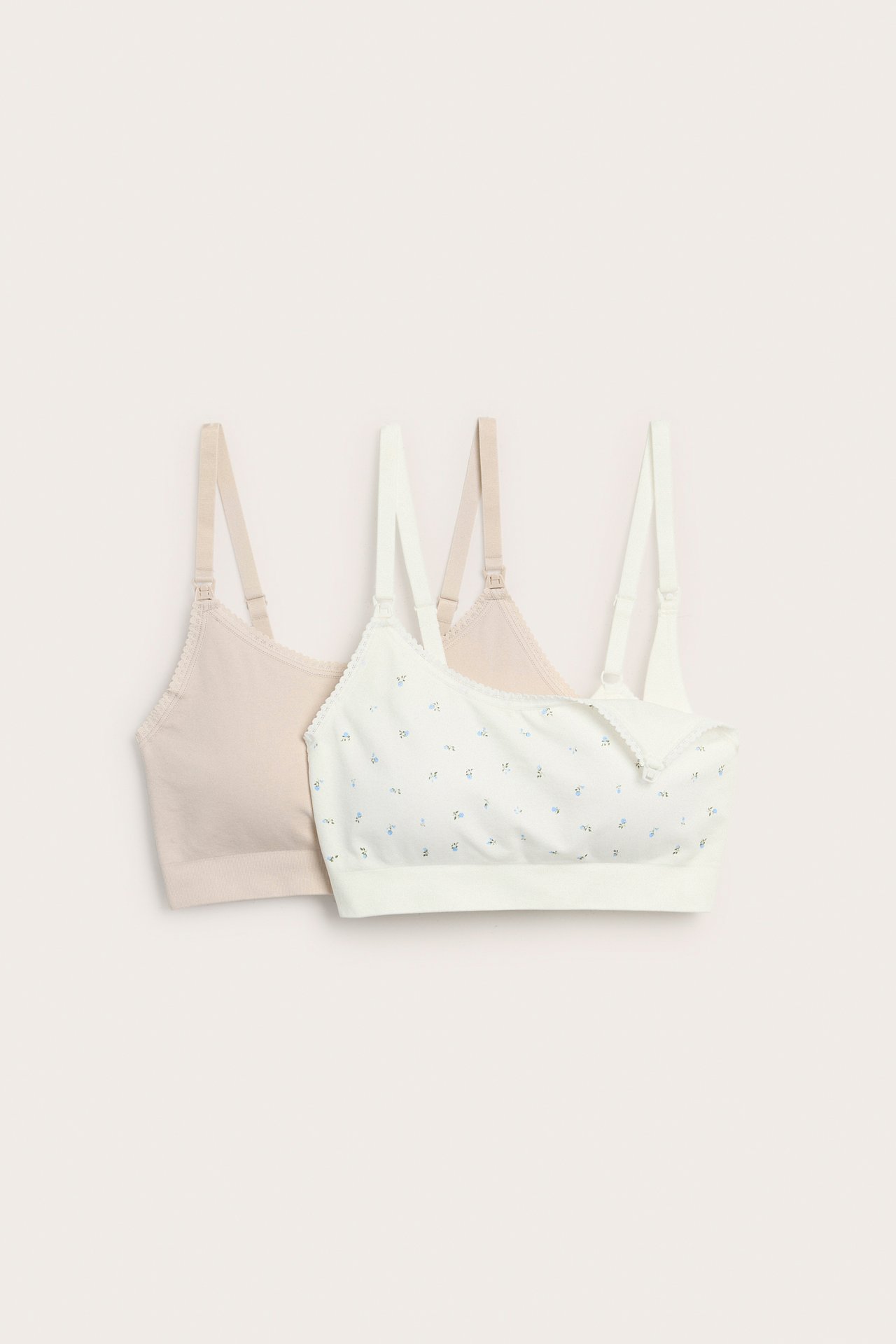Framifrån, två amnings-BH:ar för dam: en offwhite blommig, en enfärgad beige.