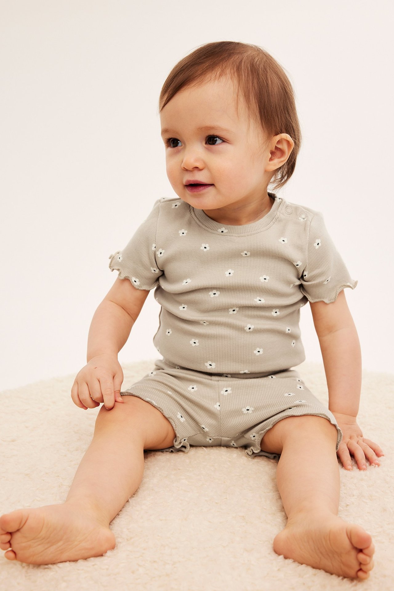 Edestä, vauva yllään beiget ribatut kukkakuosiset pyöräilyshortsit ja yhteensopiva lyhythihainen toppi.