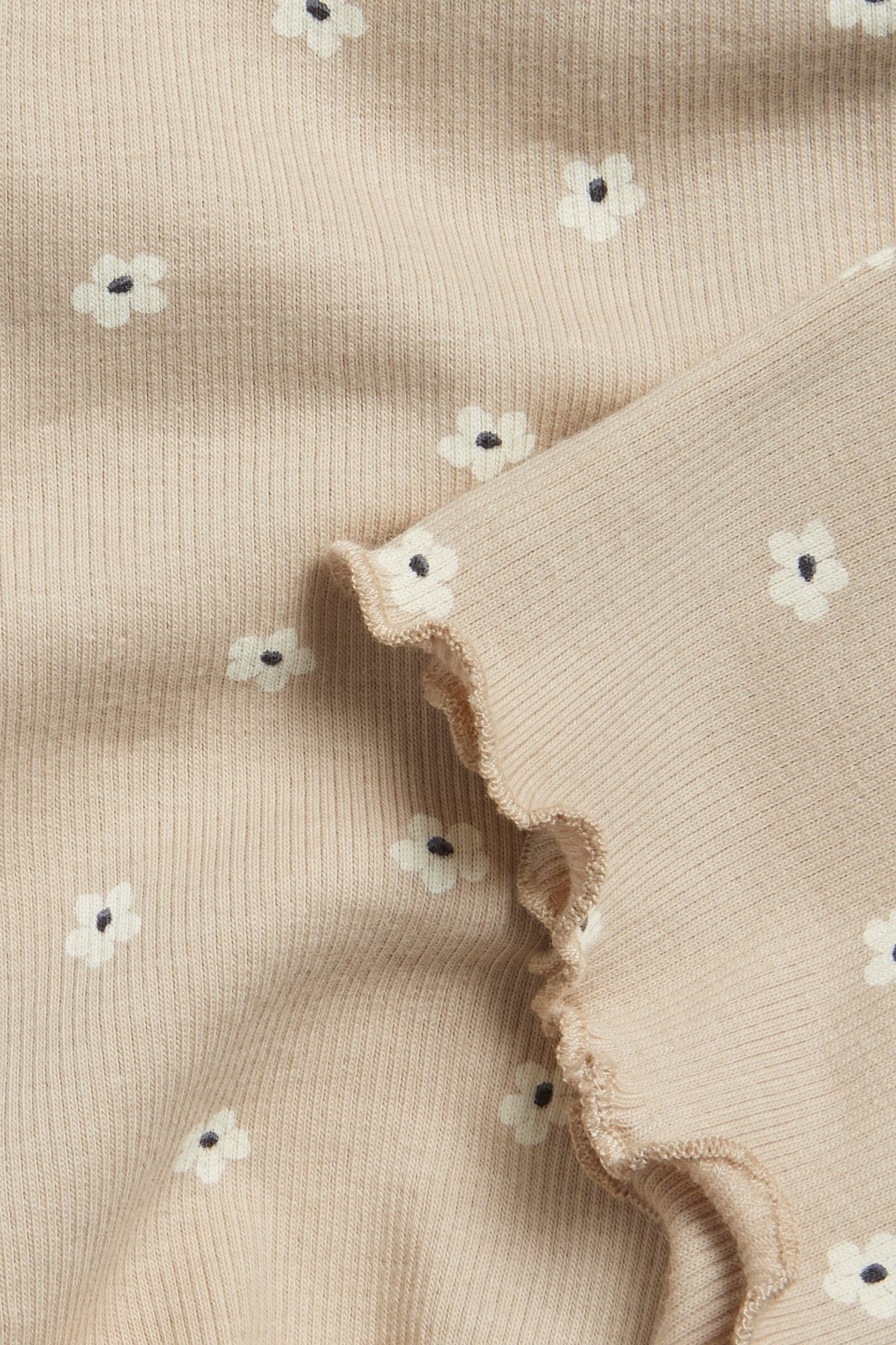 Zbliżenie beżowych prążkowanych szortów rowerowych z białym kwiatowym wzorem i falbanką.