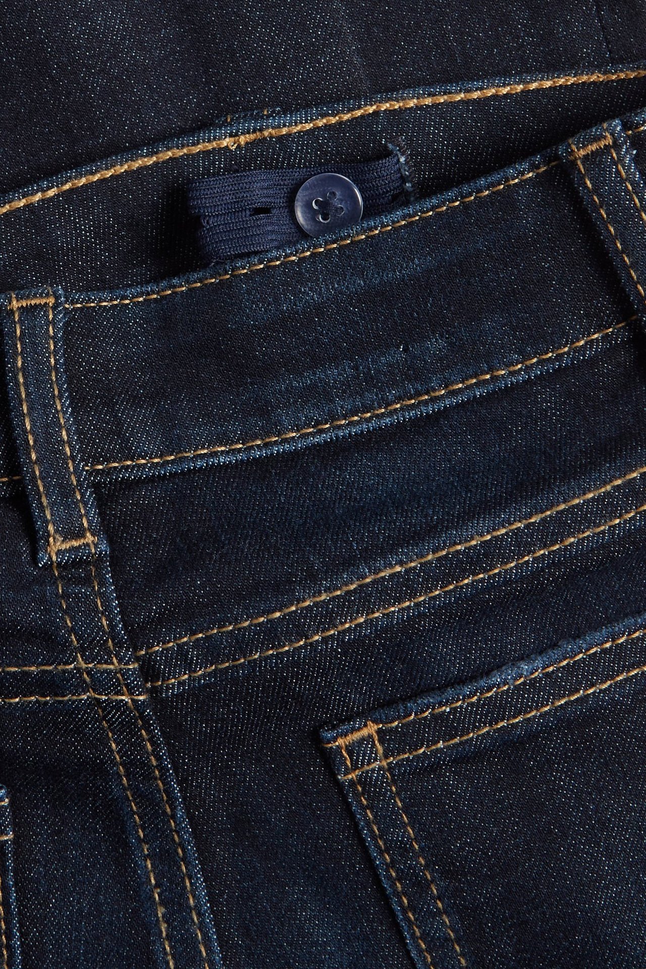 Zbliżenie na ciemnoniebieskie jeansy bootcut dla dzieci z regulowaną gumką w pasie i niebieskim guzikiem.