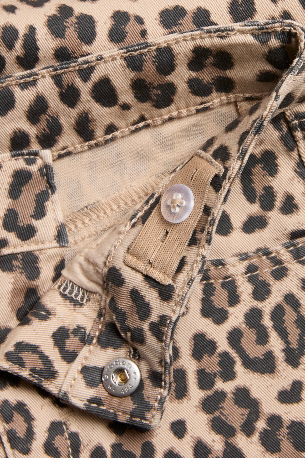 Zbliżenie na beżowe jeansy bootcut w panterkę dla dzieci z regulowaną talią i zatrzaskiem.