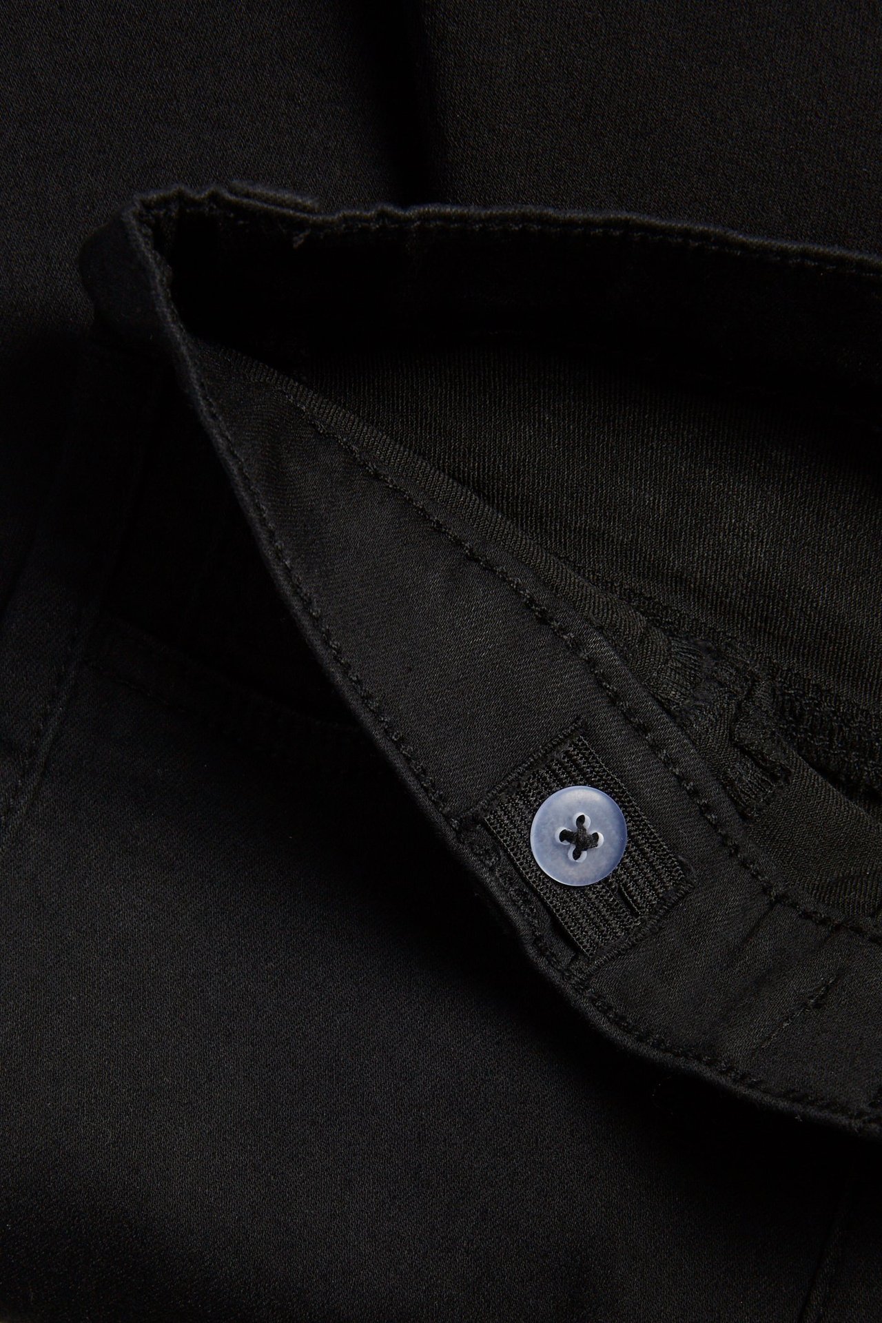 Zbliżenie na czarne jegginsy slim dla dzieci, pokazujące regulowaną talię z jasnoniebieskim guzikiem.