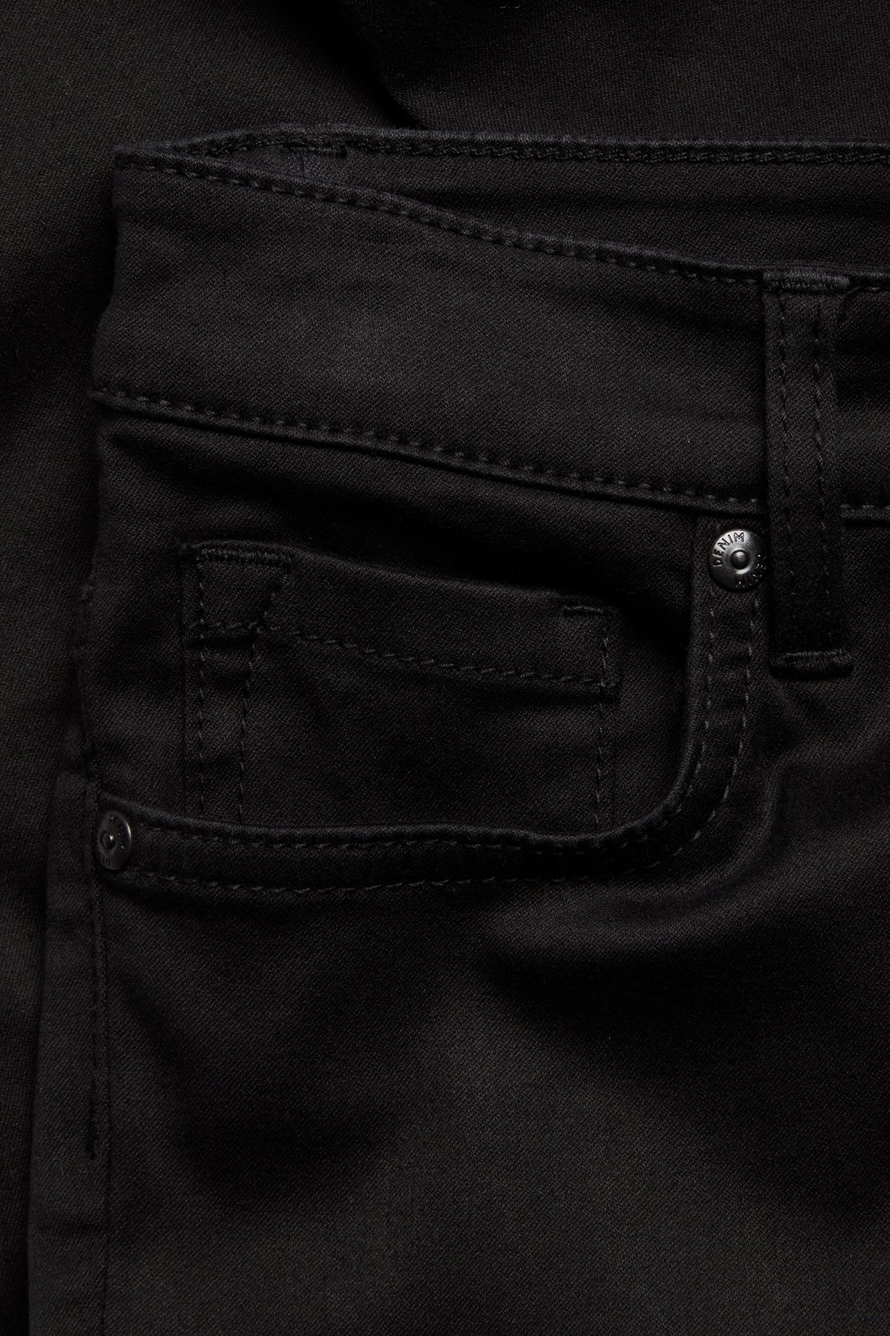 Zbliżenie z przodu czarnych jeansów Super Slim, pokazujące przednią kieszeń z małą kieszonką i guzikiem.