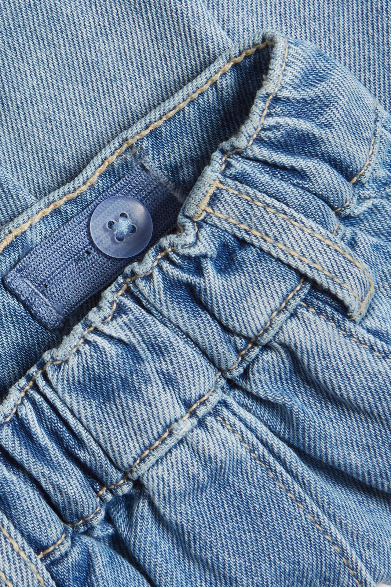 Zbliżenie na jasnoniebieską spódnicę jeansową z elastycznym pasem i niebieskim guzikiem.
