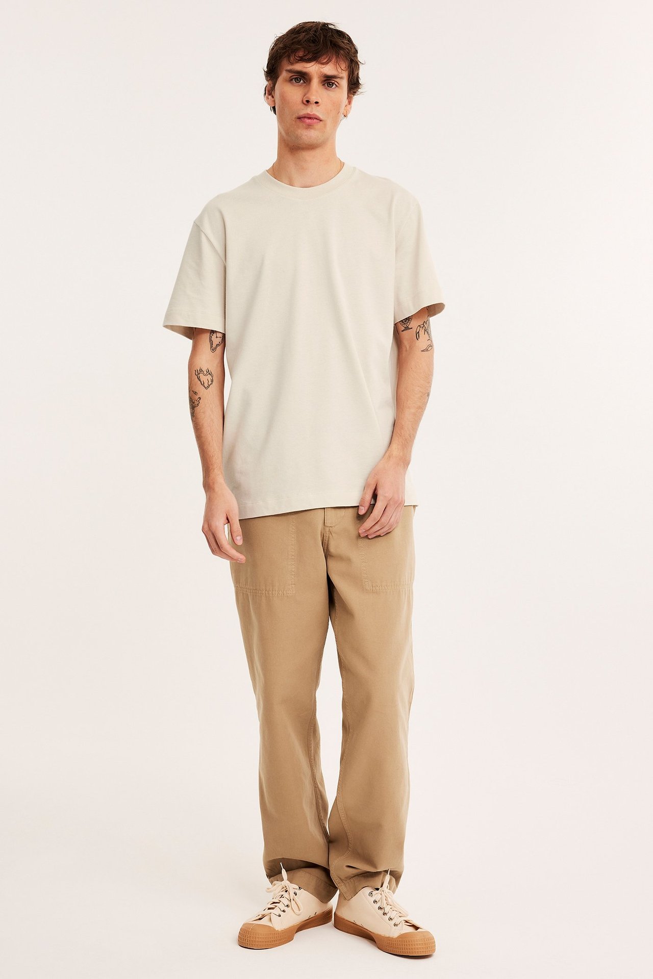 Edestä kuvattu mies yllään vaaleanbeige rento puuvillapaita, khakihousut ja vaaleanbeiget tennarit.