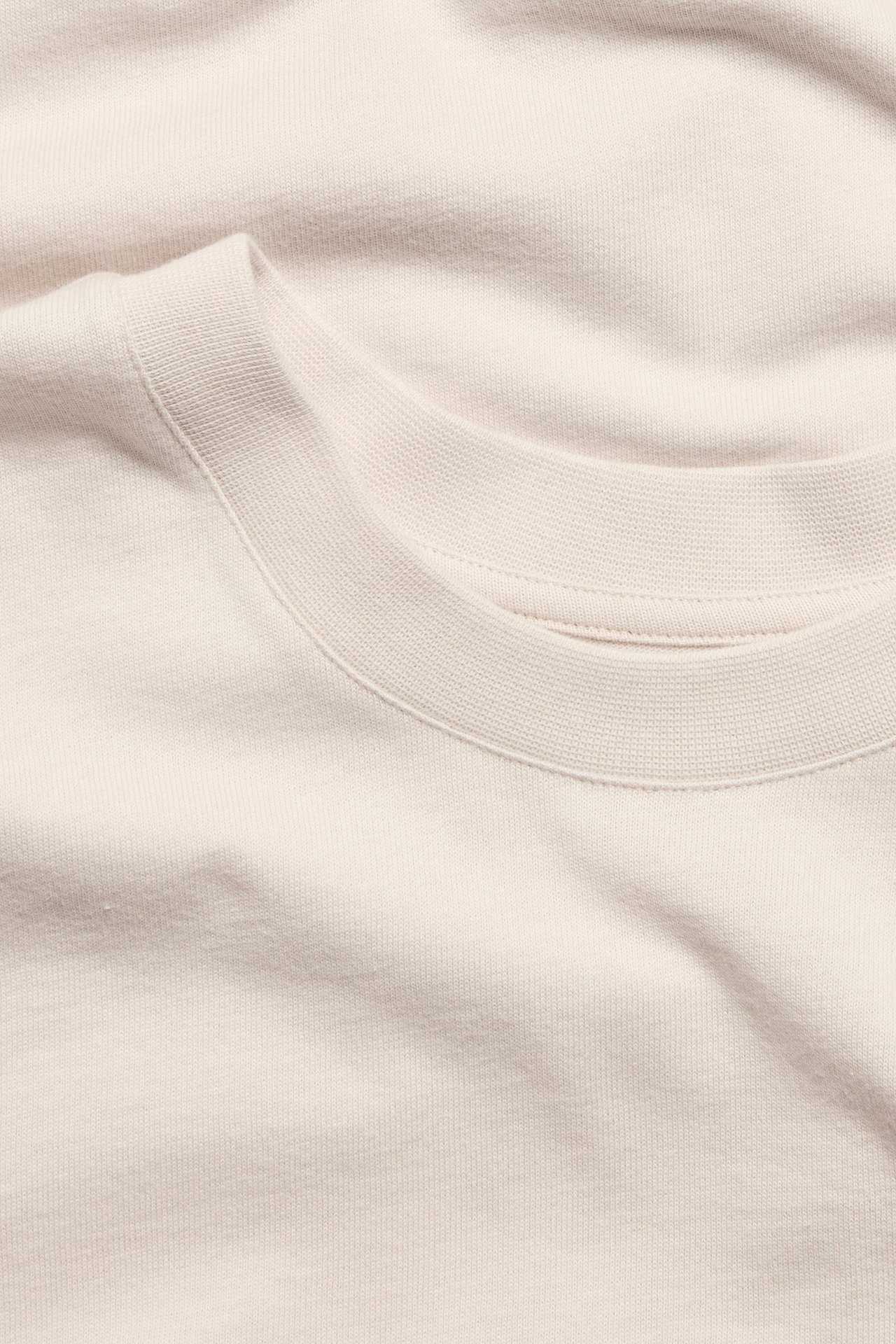 Zbliżenie na jasnobeżowy, gładki, bawełniany t-shirt z okrągłym dekoltem i luźnym krojem.