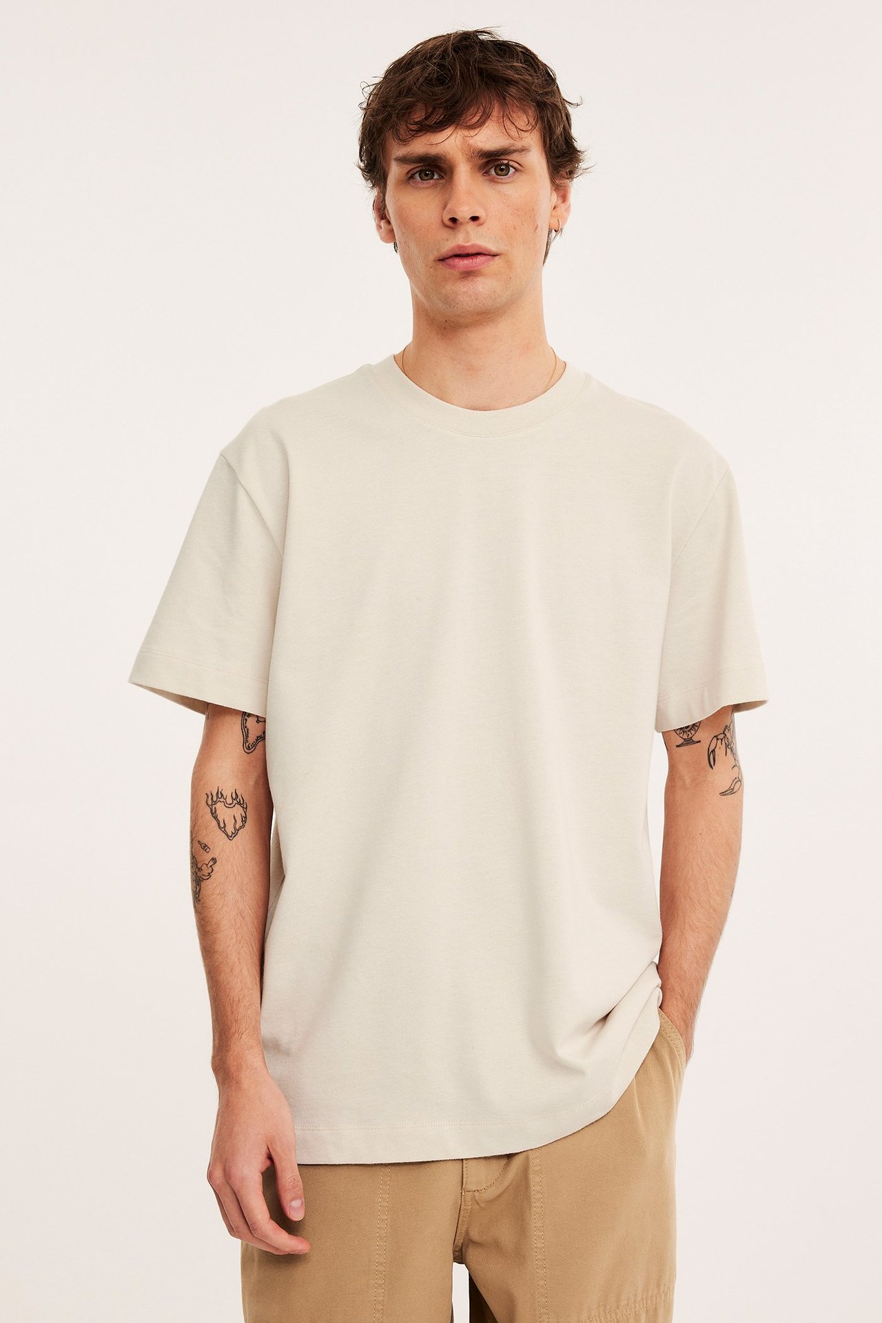 Frontbilde av en mann i en lys beige oversized bomulls-t-skjorte med rund hals og beige shorts.