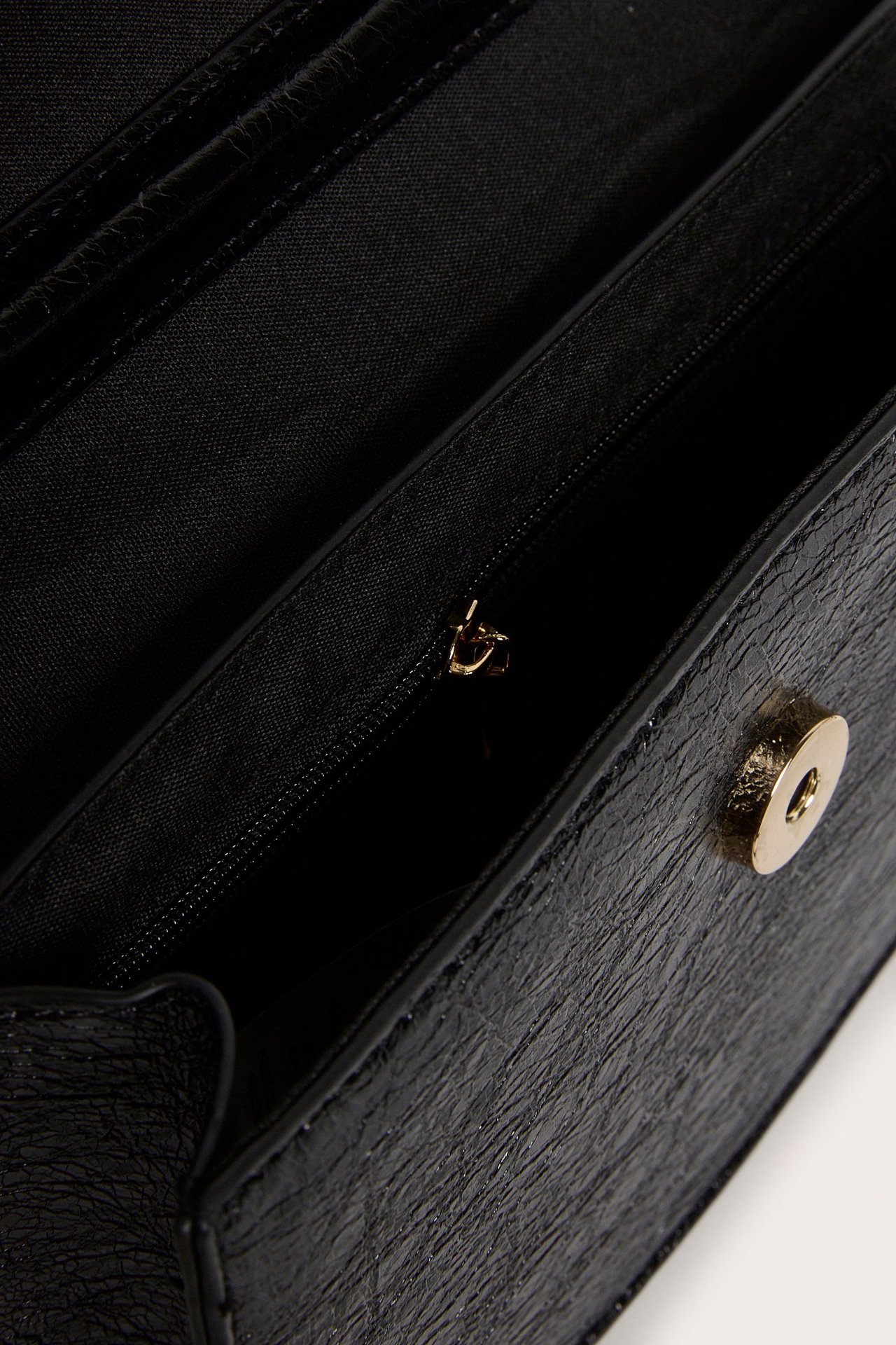 Zbliżenie otwartej czarnej teksturowanej torebki na ramię ze sztucznej skóry, z wewnętrzną kieszenią i złotym zapięciem.