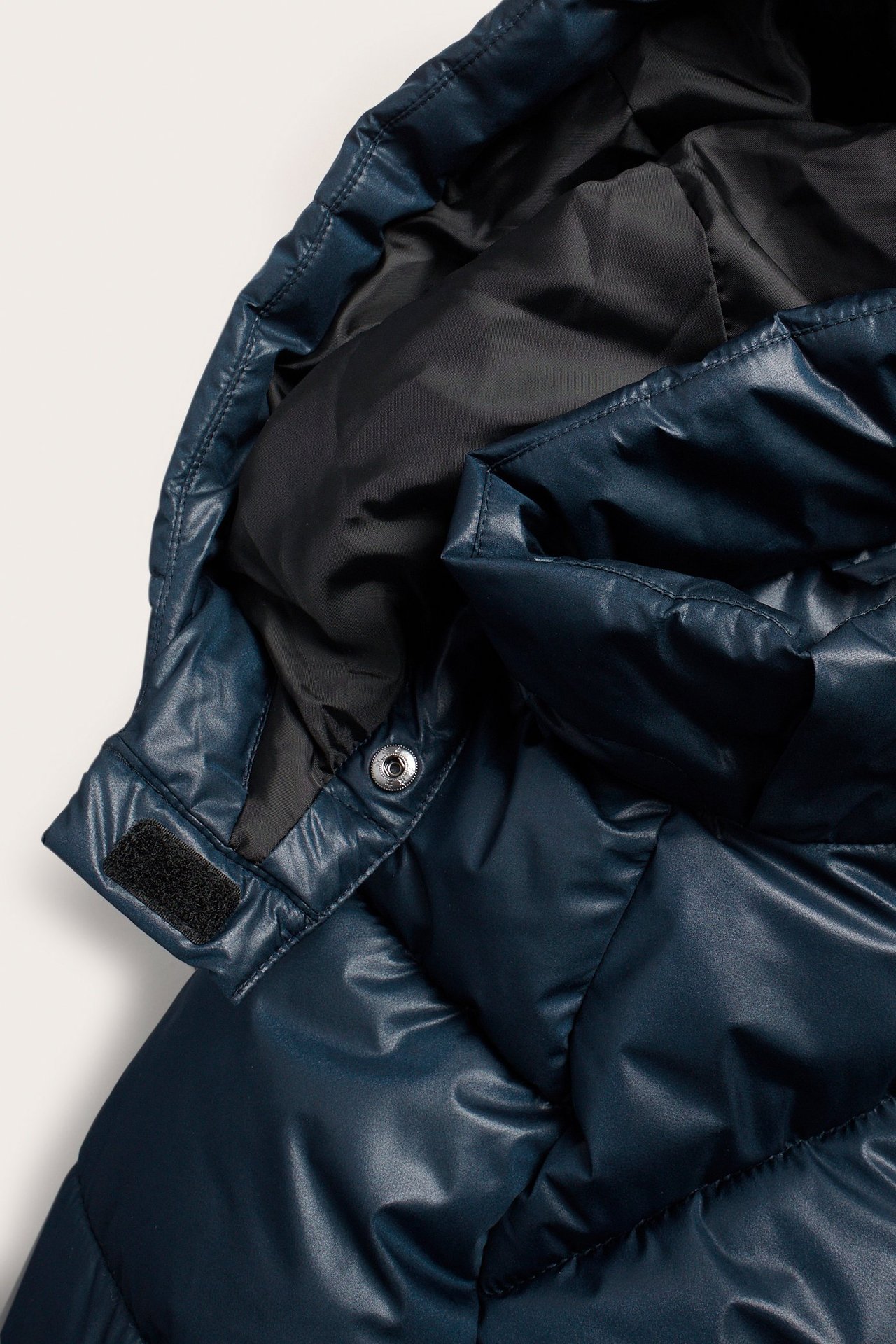 Zbliżenie na granatową, półbłyszczącą kurtkę puchową dziecięcą z odpinanym kapturem, widoczny zatrzask i rzep.