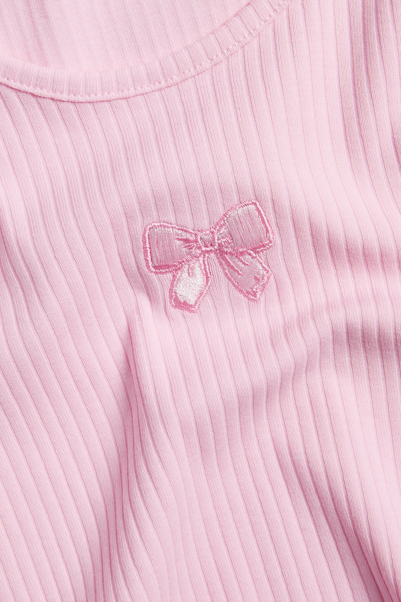 Närbild av en rosa ribbad topp med en rosa broderad rosett.