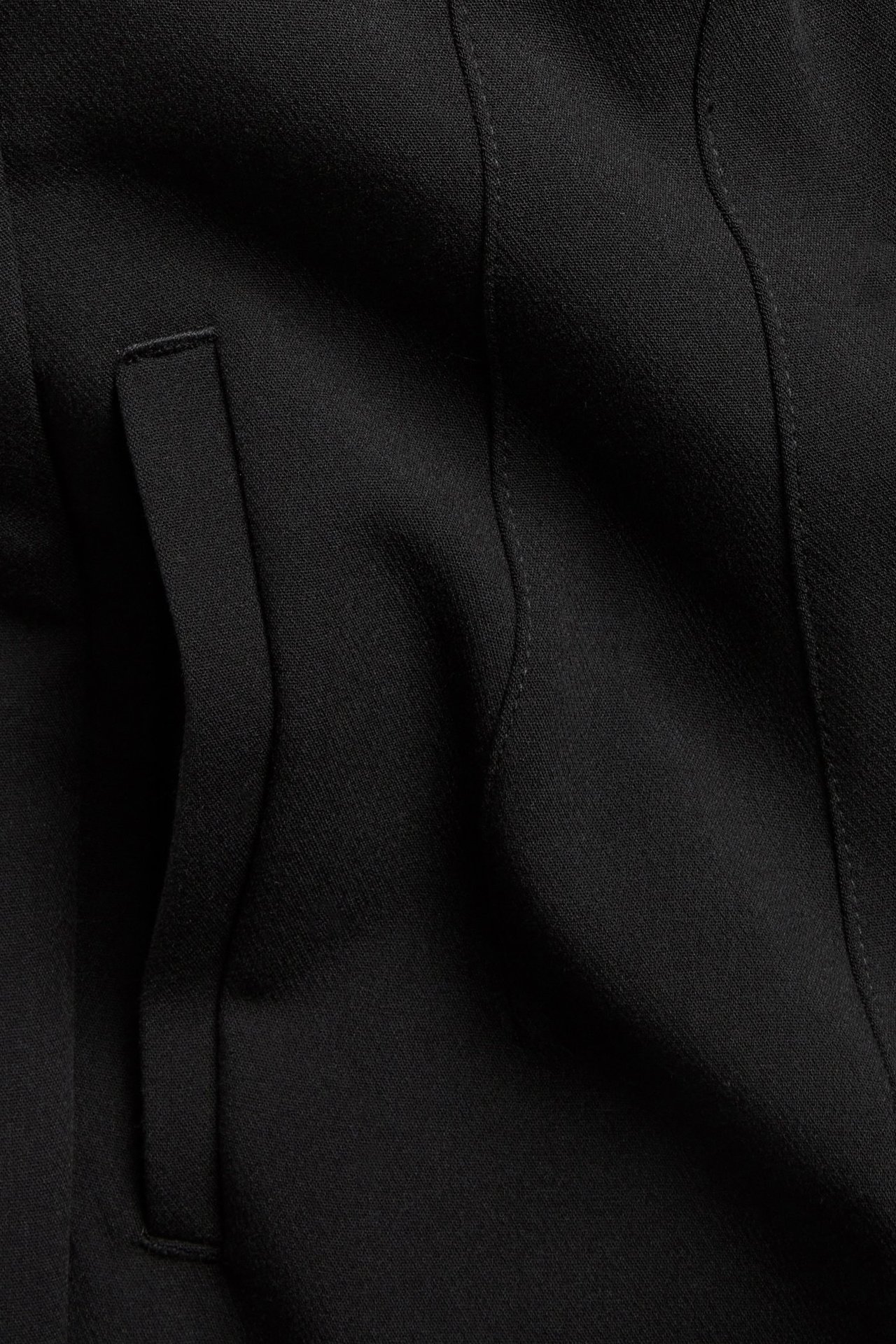 Zbliżenie czarnego materiału spodni garniturowych, ukazujące szew lub detal kieszeni.