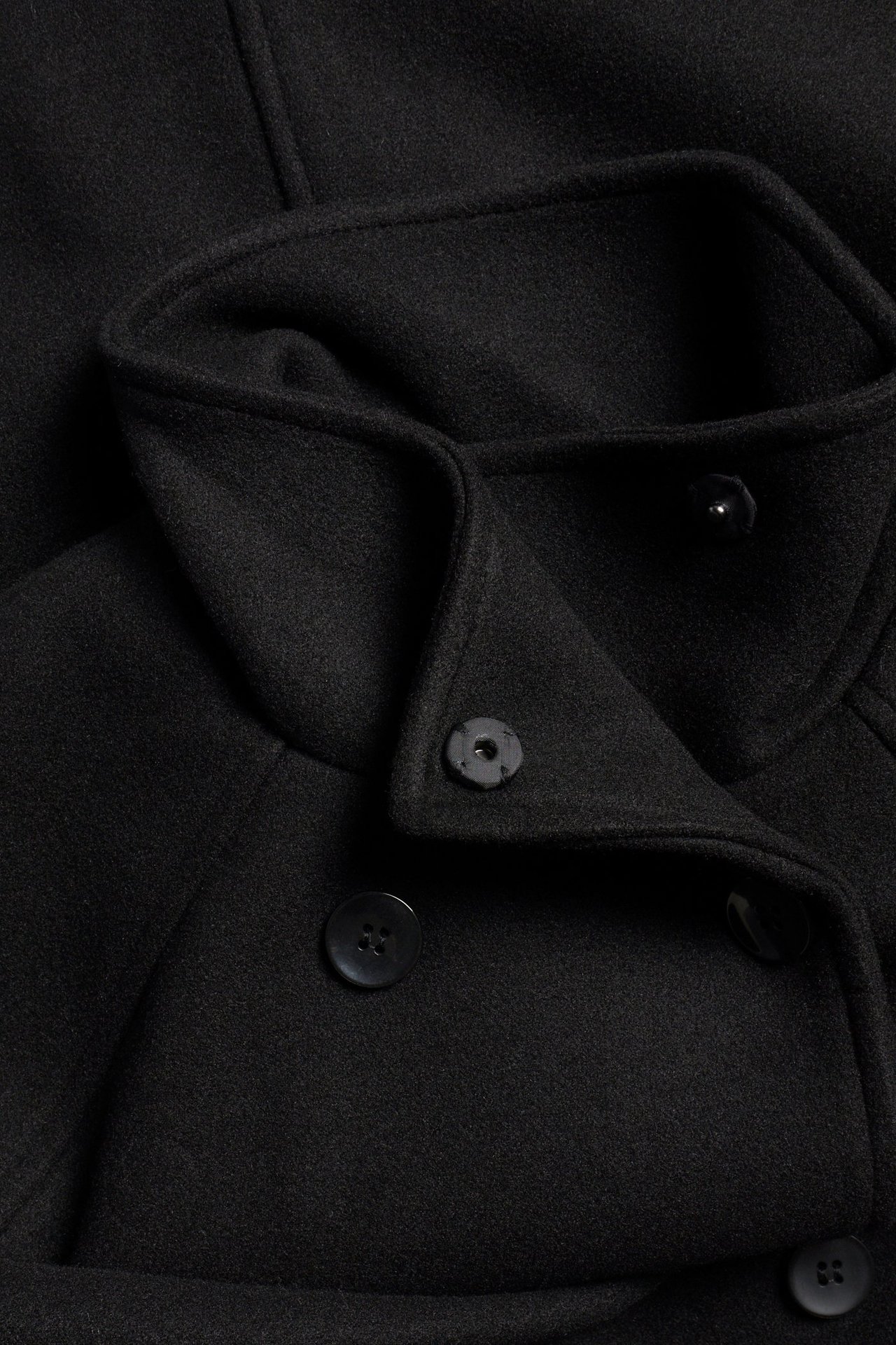 Zbliżenie czarnej, dwurzędowej kurtki z szerokim kołnierzem i czarnymi guzikami.