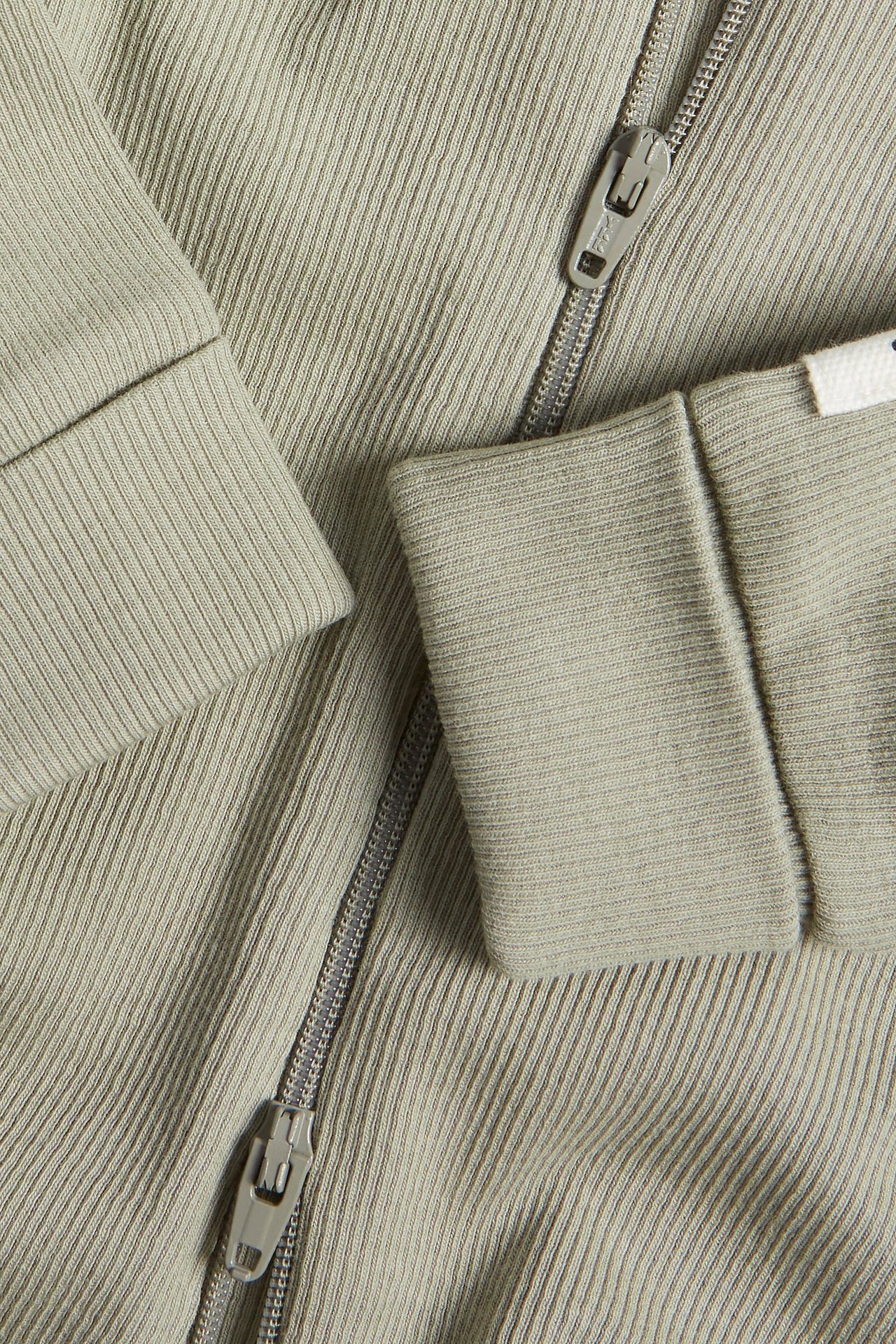 Zbliżenie na ciemnozielony prążkowany kombinezon niemowlęcy z dwukierunkowym zamkiem błyskawicznym i wywiniętymi mankietami.