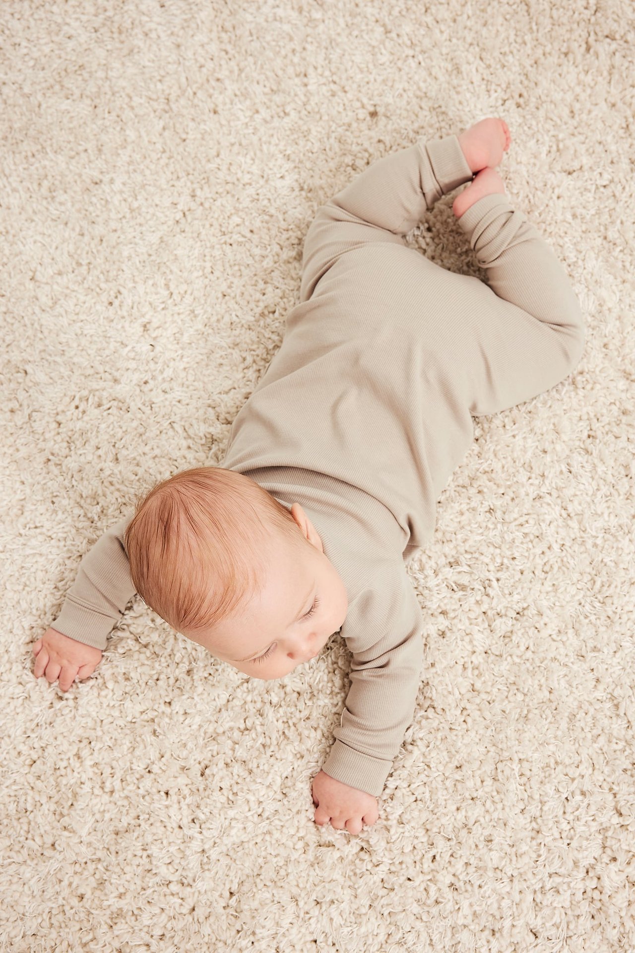 Uppifrån sett en baby i en ljusbeige ribbad långärmad heldress.