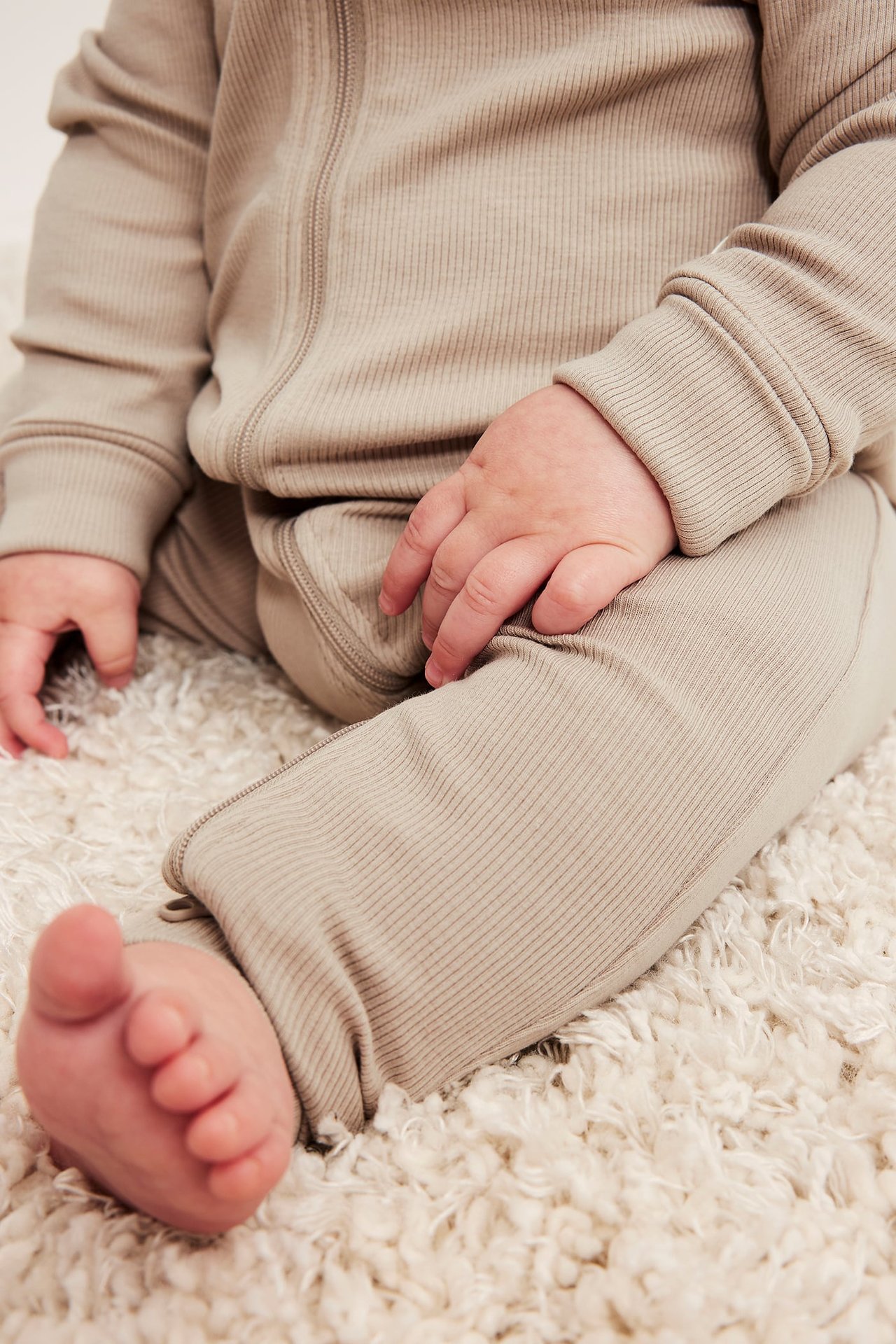 Närbild på en baby i en ribbad beige sparkdräkt med dragkedja fram.
