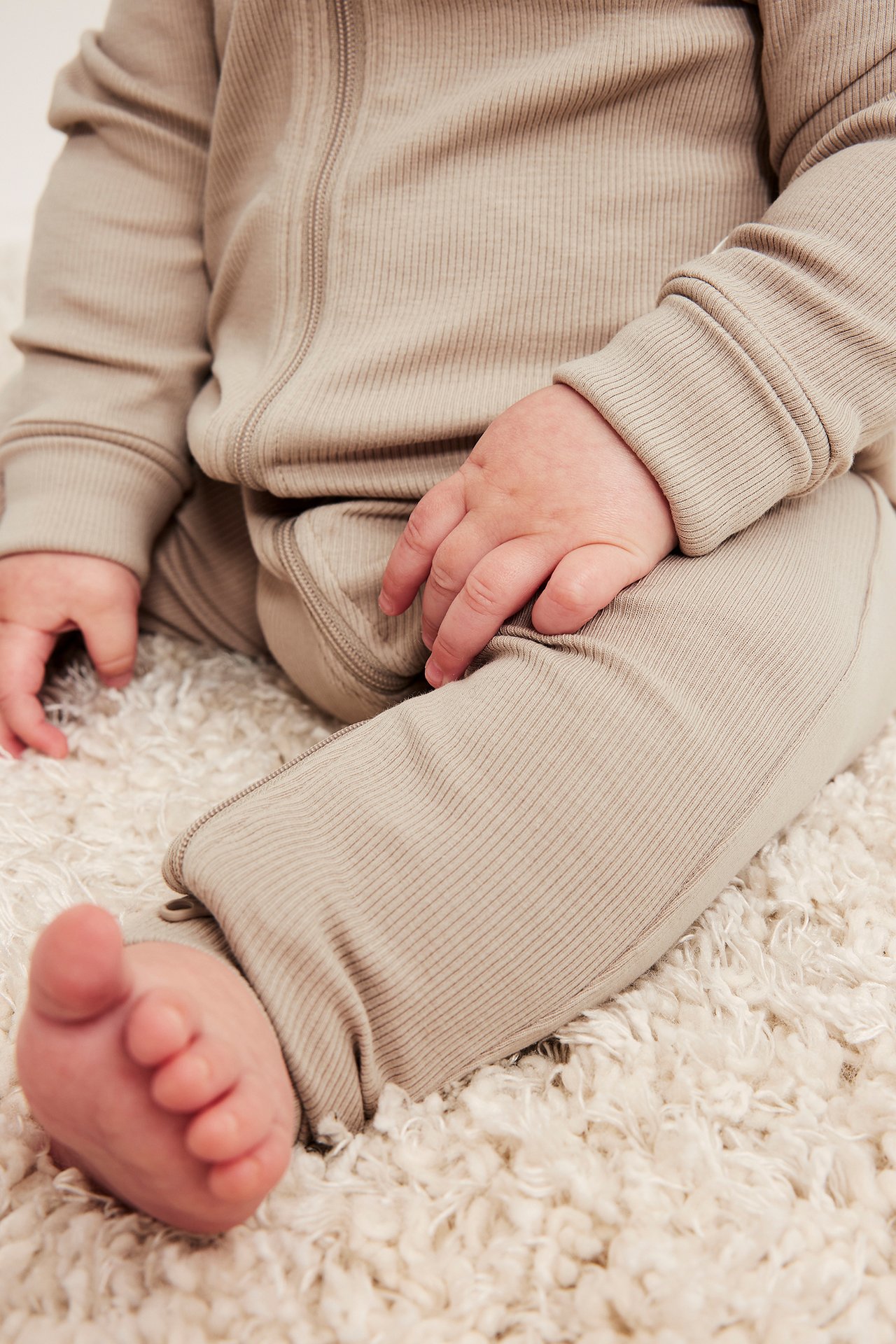 Nærbilde av en baby i en ribbet beige heldress med glidelås foran.