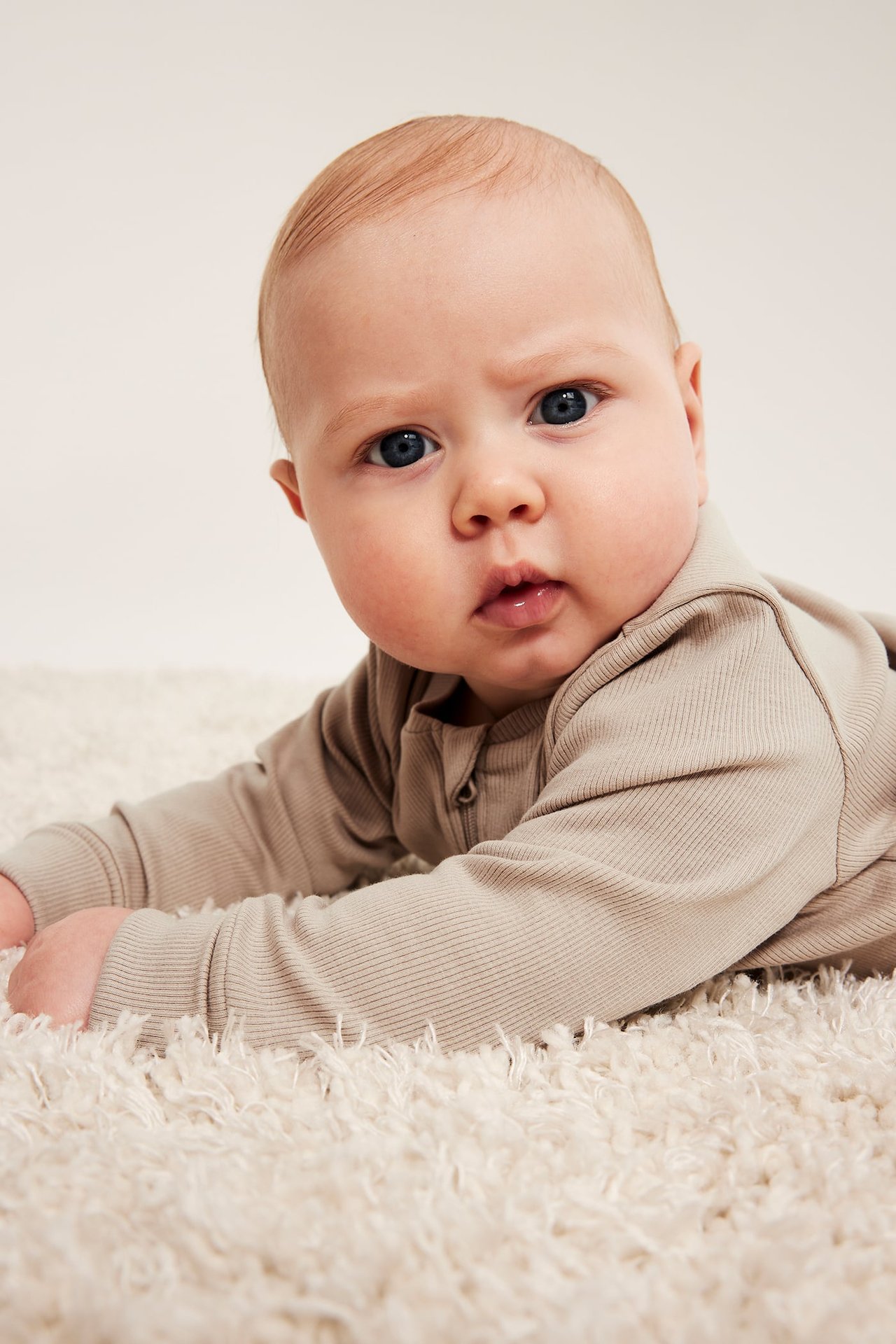Närbild framifrån av en baby i en beige ribbad långärmad body.