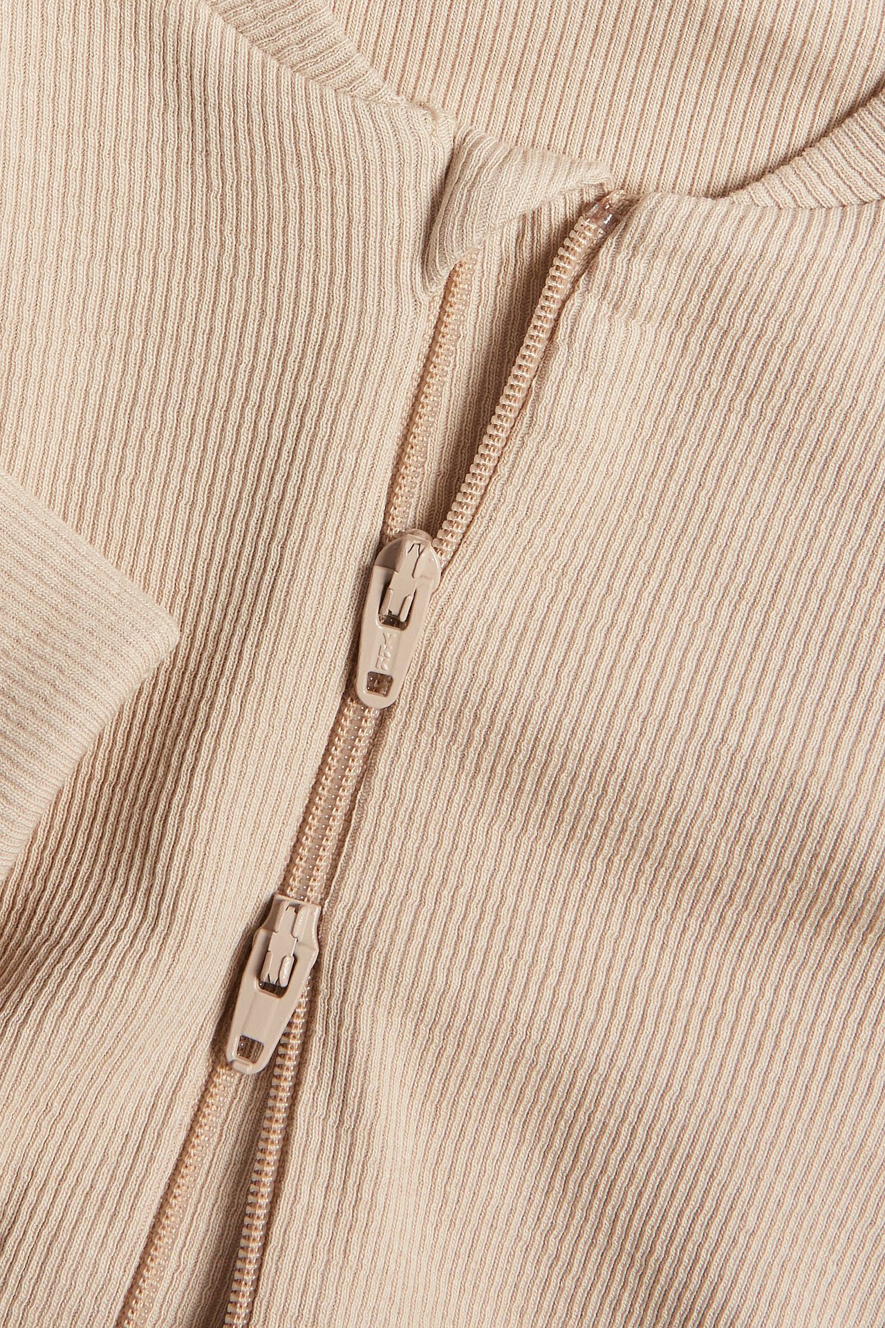 Zbliżenie beżowego, prążkowanego kombinezonu niemowlęcego z dwukierunkowym zamkiem błyskawicznym.