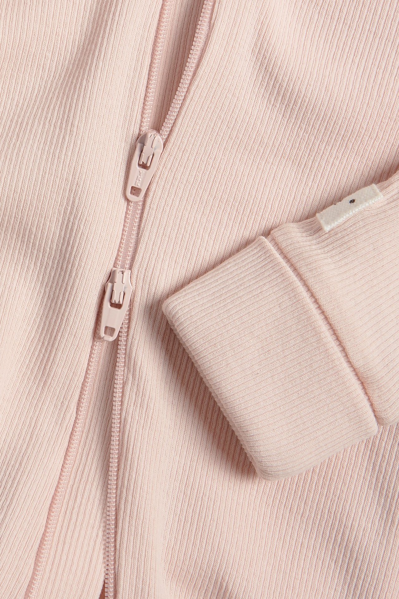 Zbliżenie różowego prążkowanego pajacyka niemowlęcego z dwukierunkowym zamkiem błyskawicznym i wywiniętym mankietem.