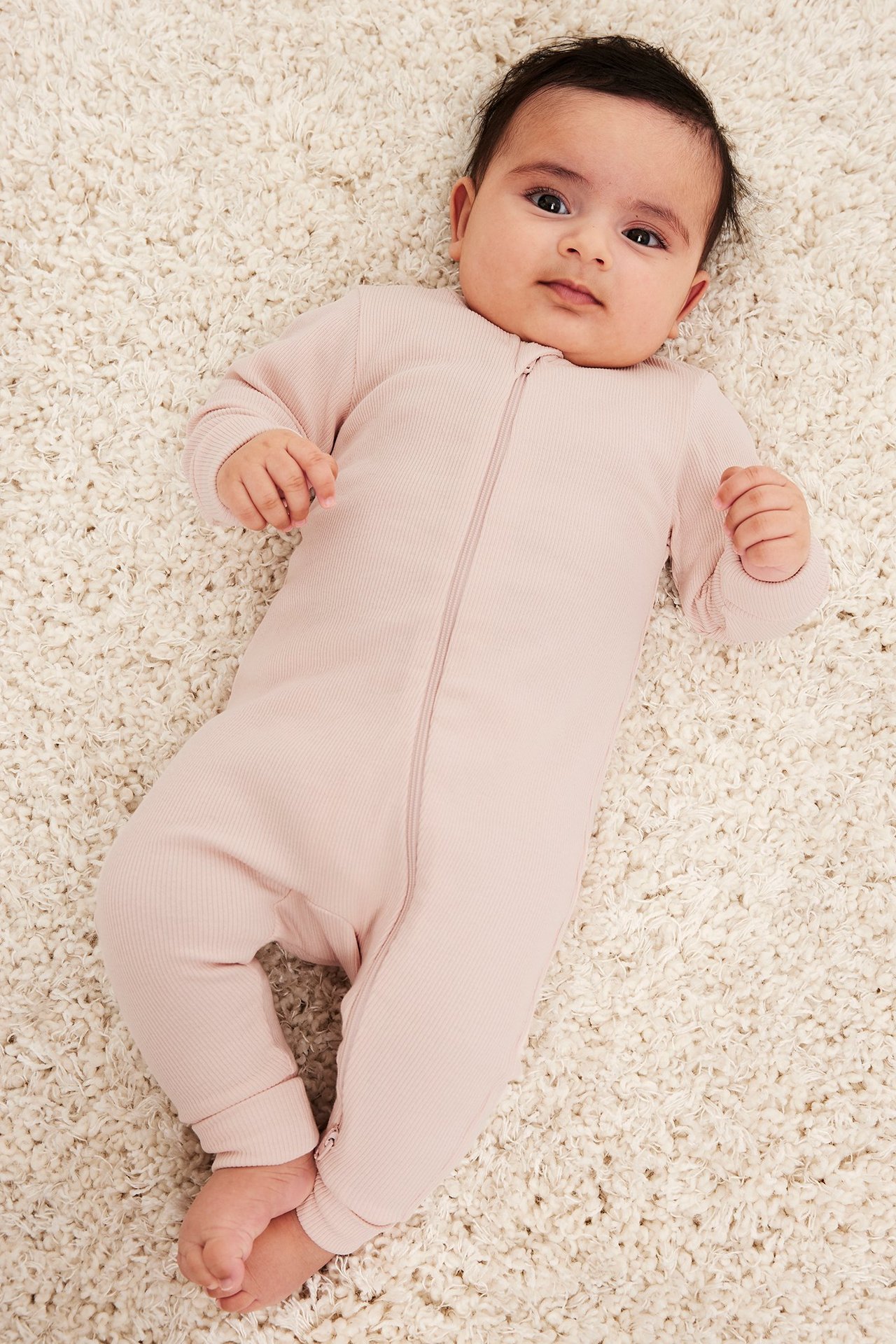 Uppifrån-vy av en baby i en rosa ribbad långärmad jumpsuit med tvåvägsdragkedja fram.