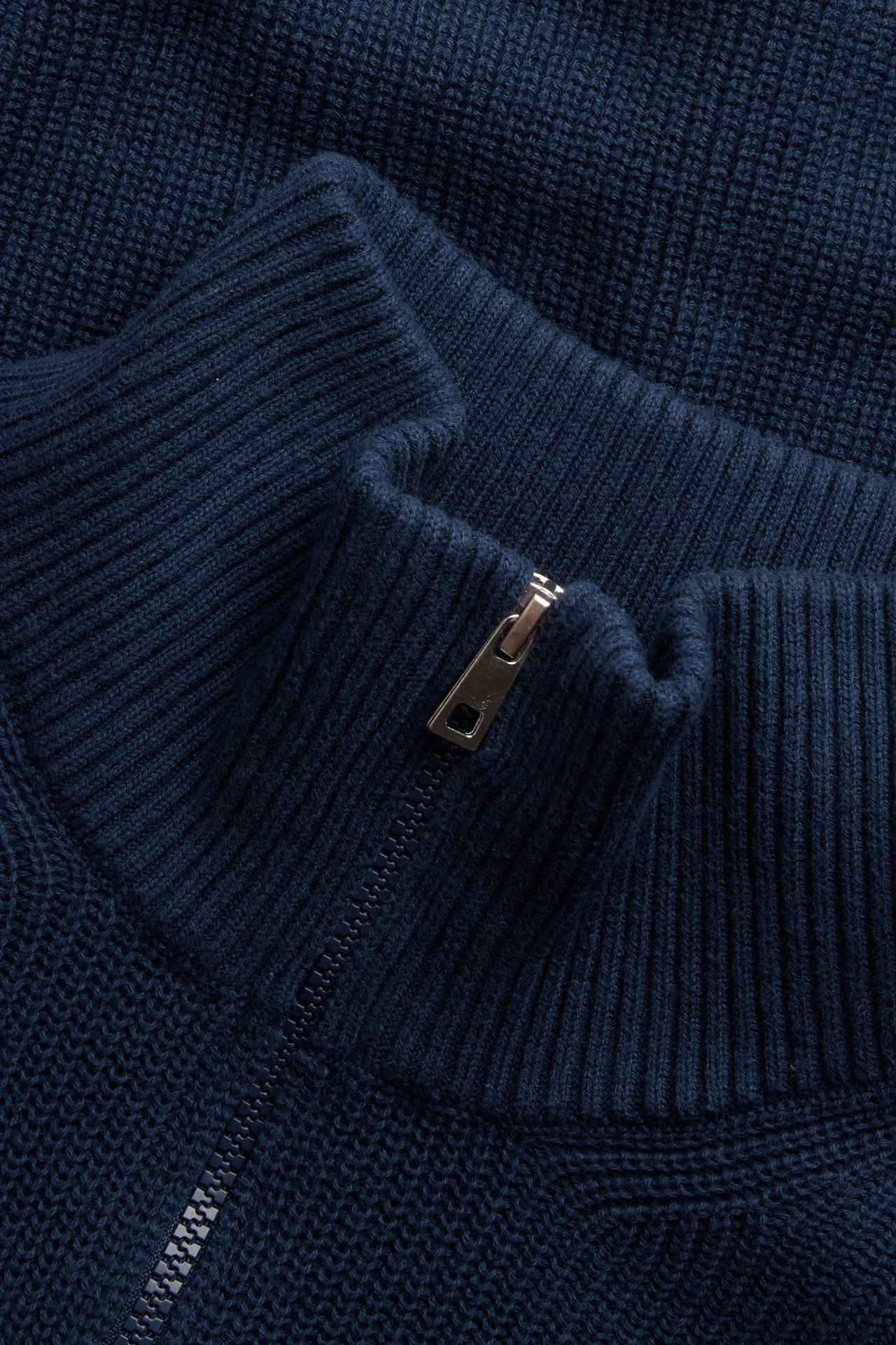 Zbliżenie na ciemnoniebieski dziergany bawełniany sweter z pół-zamkiem, ściągaczowym kołnierzem i srebrnym zamkiem.
