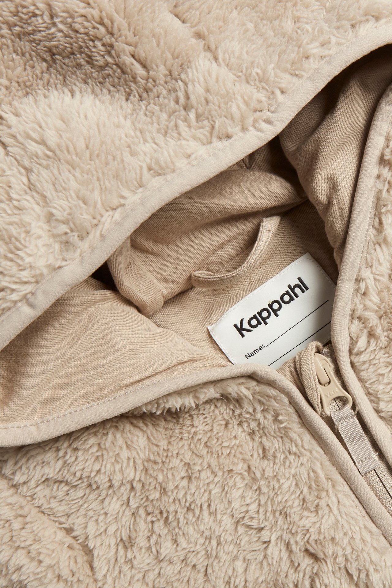 Zbliżenie beżowego pajacyka niemowlęcego z polaru, z zamkiem błyskawicznym i bawełnianą podszewką w kapturze.