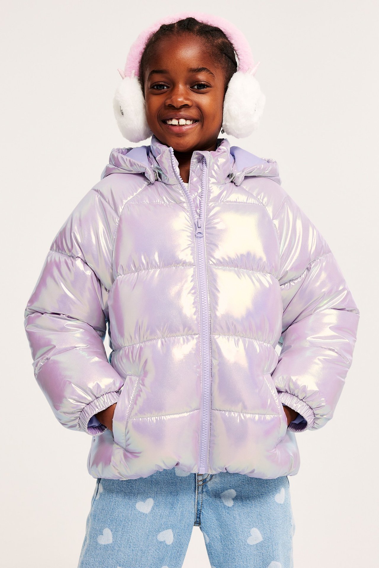 Framifrån: Barn i skimrande ljuslila pufferjacka, hjärtmönstrade jeans och rosa lurviga hörselkåpor.