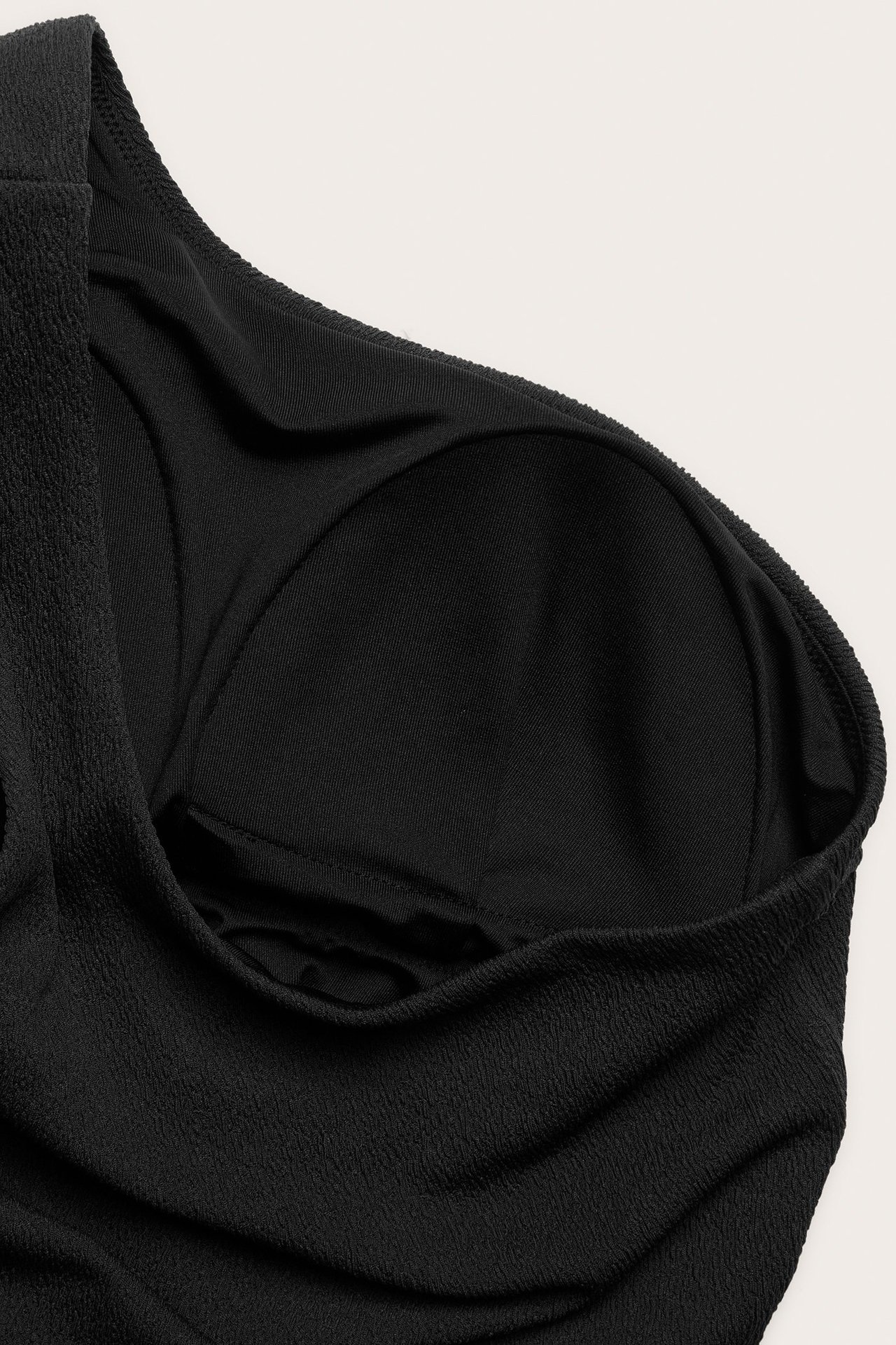 Zbliżenie czarnego jednoramiennego kostiumu kąpielowego z teksturowanej tkaniny i widoczną wyściełaną miseczką.