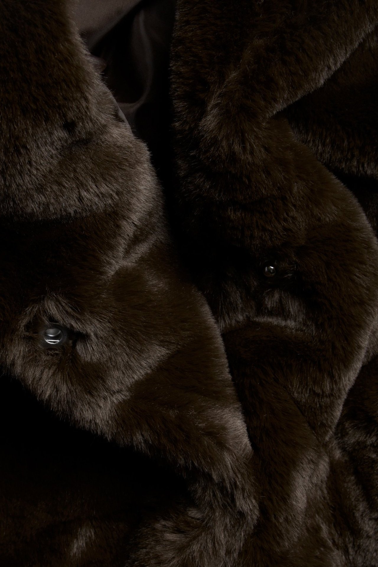 Zbliżenie na ciemnobrązową kurtkę ze sztucznego futra z dużym kołnierzem i widocznymi zatrzaskami.