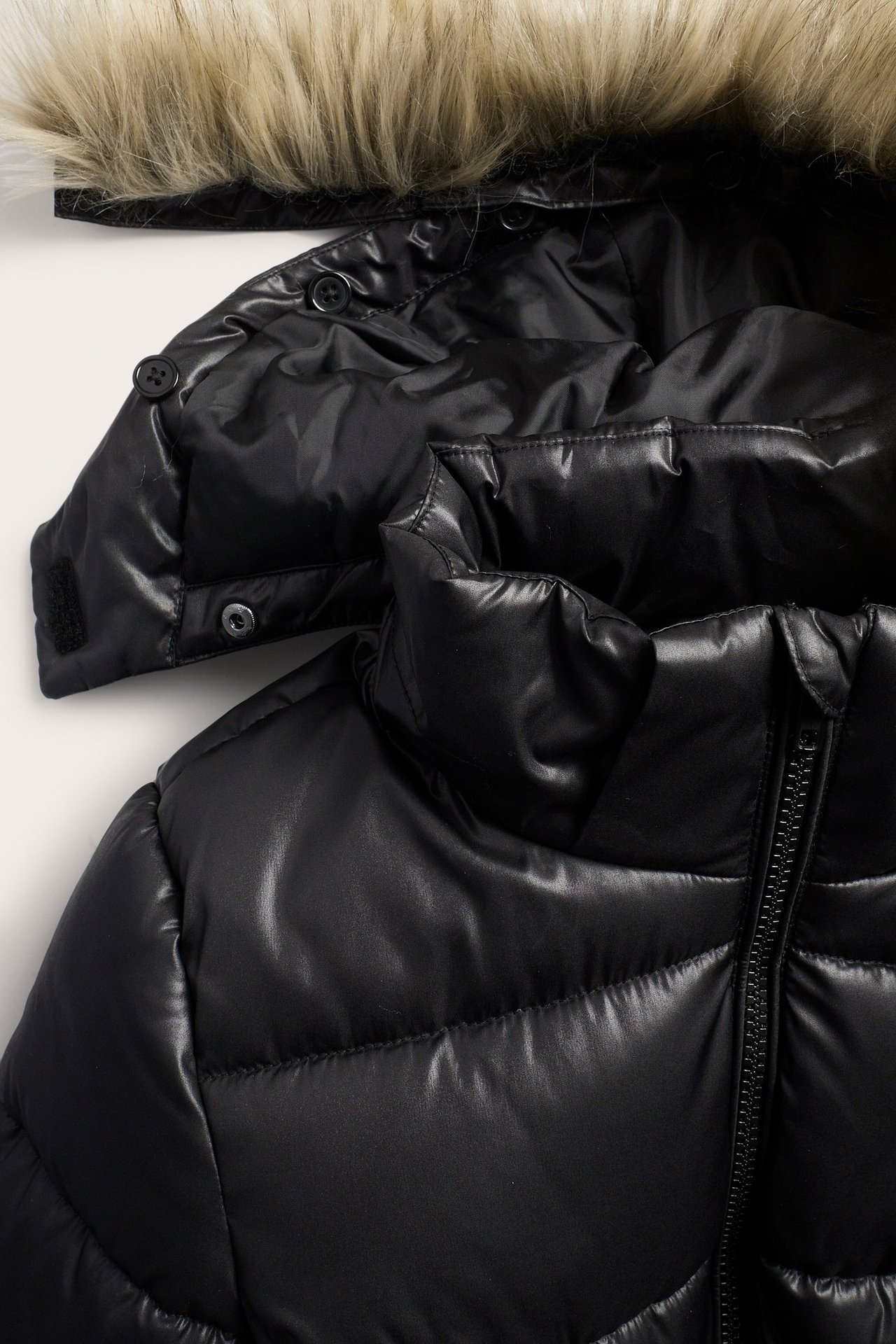 Zbliżenie czarnej kurtki puchowej z odpinanym kapturem, jasnobrązowym sztucznym futrem i zamkiem błyskawicznym.