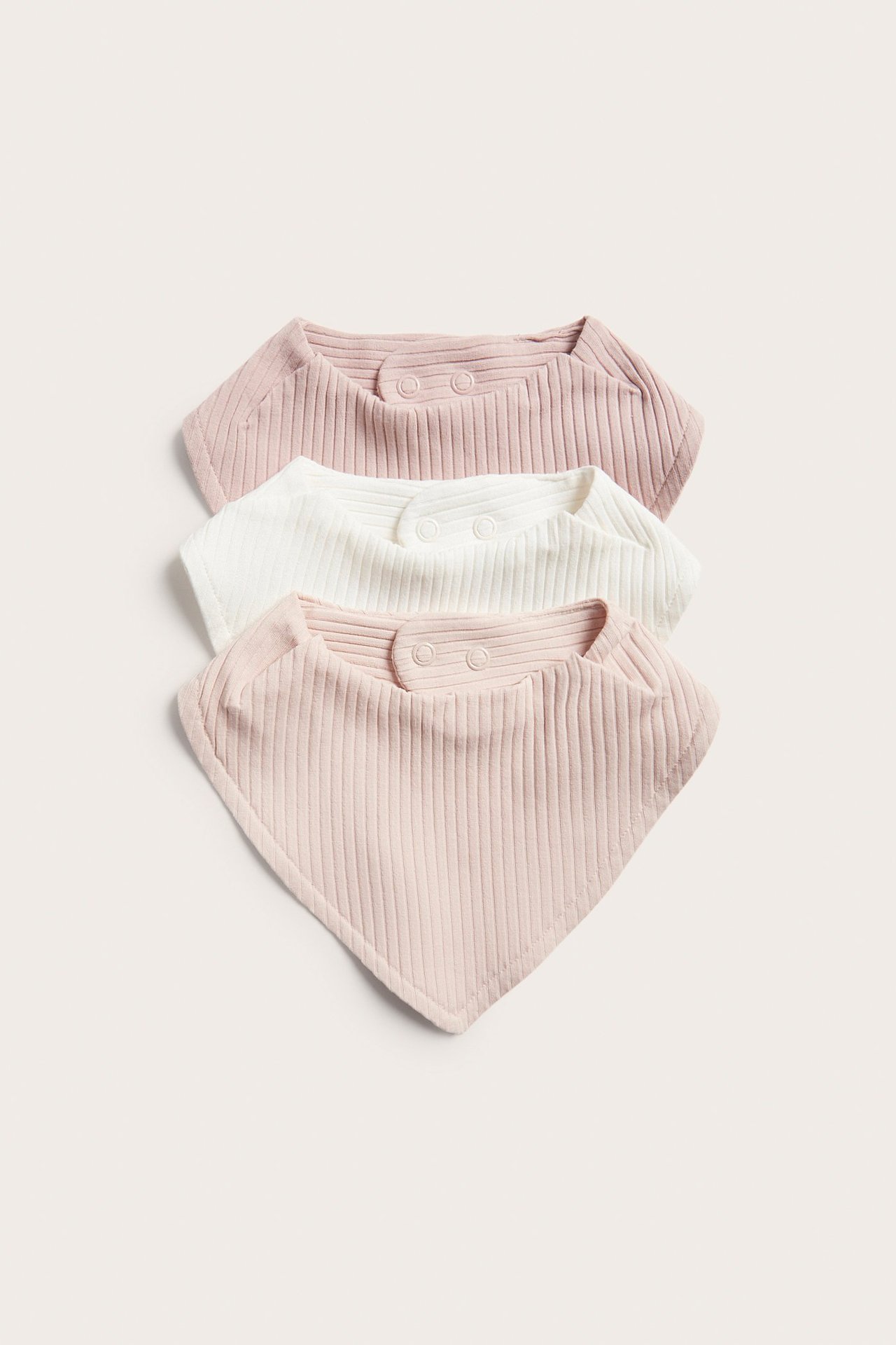Uppifrån sett, tre ribbade babyhaklappar: två ljusrosa och en benvit, alla med tryckknappsfästen.
