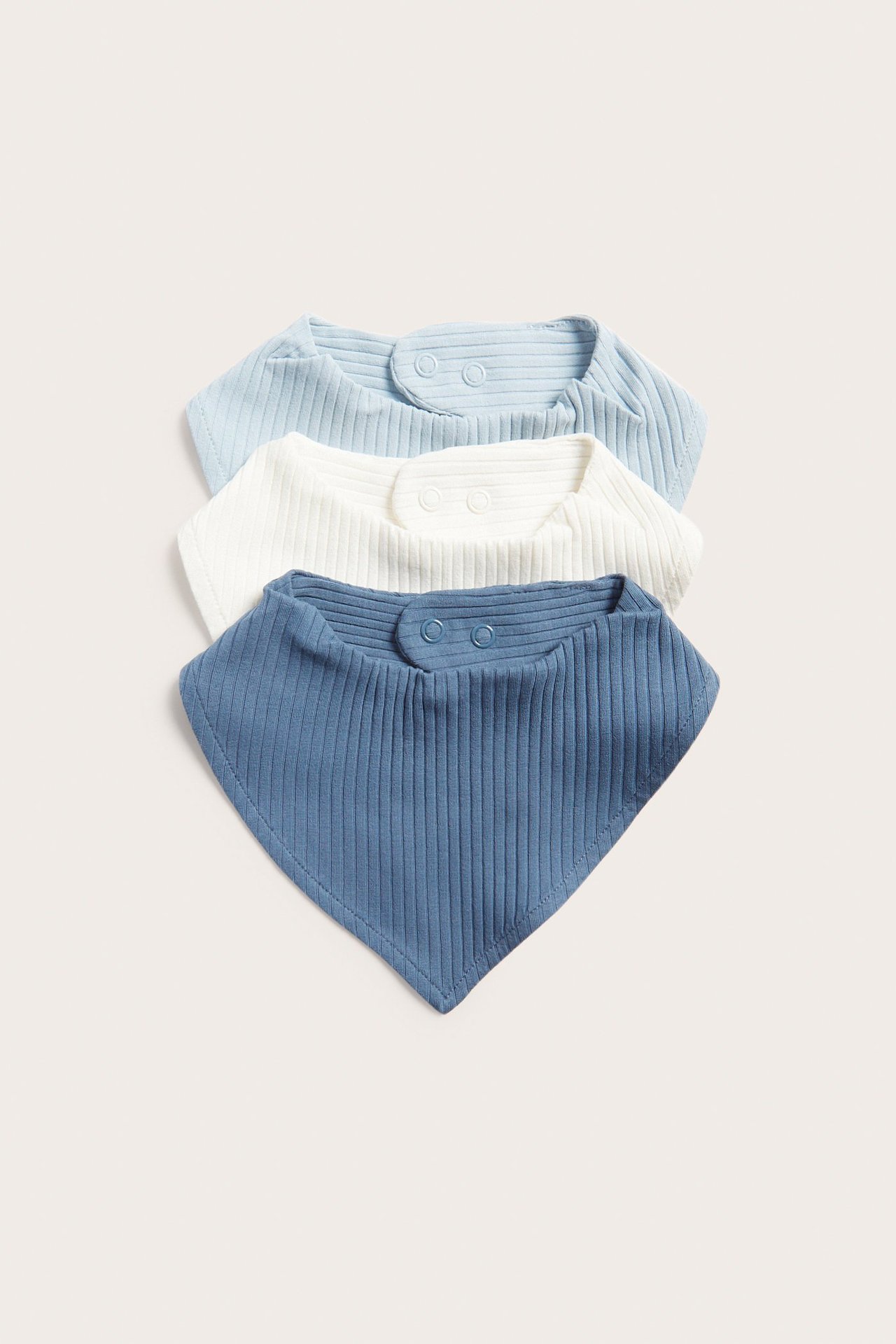 Toppvy av tre ribbade babyhaklappar: ljusblå, vit och blå, med tryckknappar.