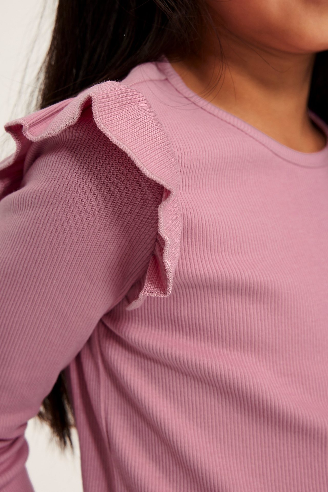 Närbild av kid i rosa ribbad långärmad topp med volanger på axeln.