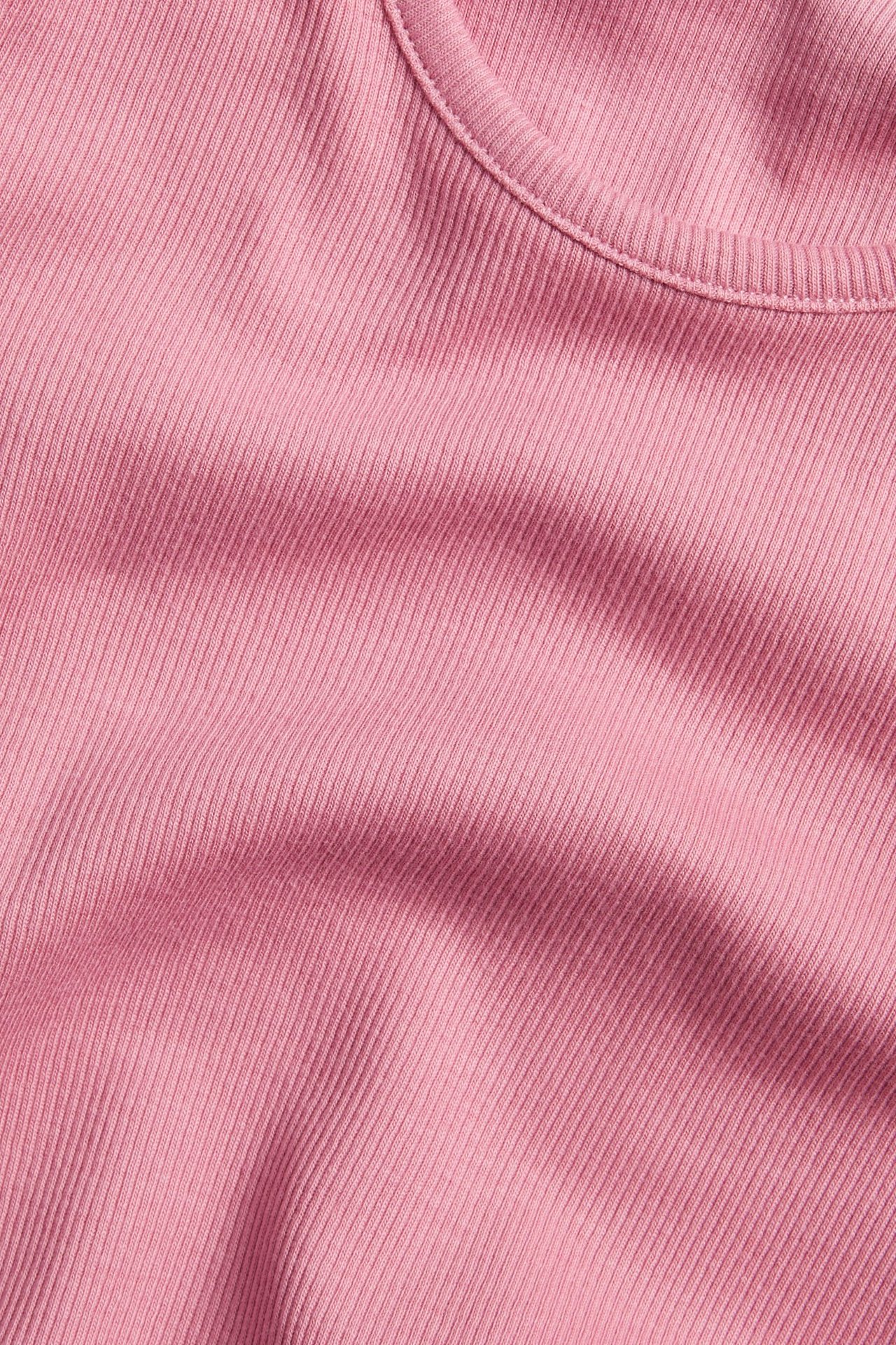 Nærbilde av en rosa ribbet langermet topp, som viser det ensfargede bomullsstoffet og halslinningen.