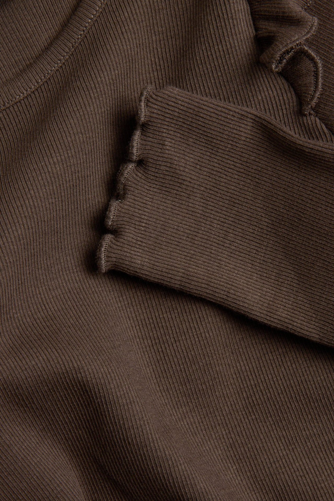 Zbliżenie na ciemnobrązowy prążkowany top z długim rękawem z falbankami przy mankietach i dekolcie.