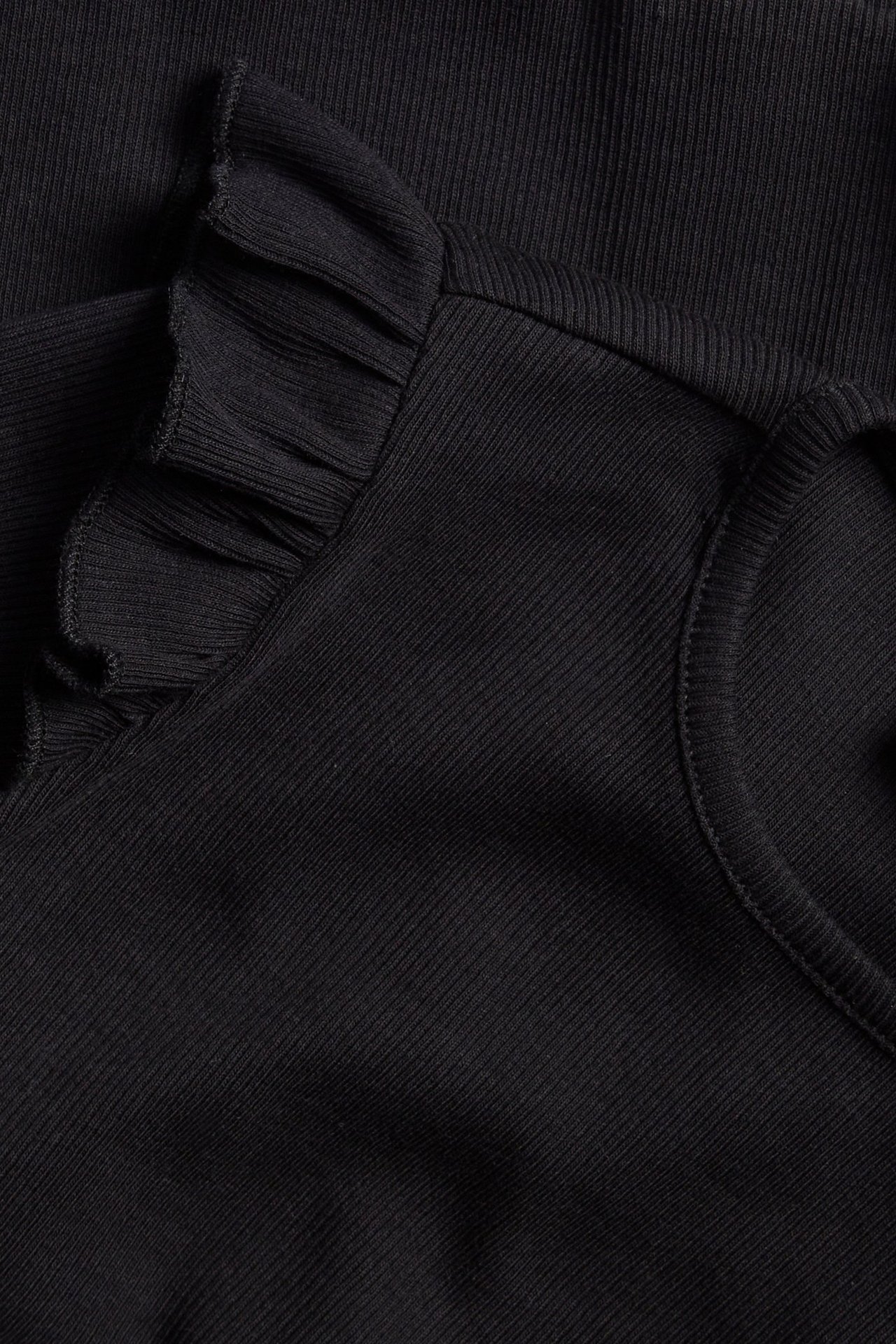 Zbliżenie na czarny prążkowany top z długim rękawem i falbanką na ramieniu.