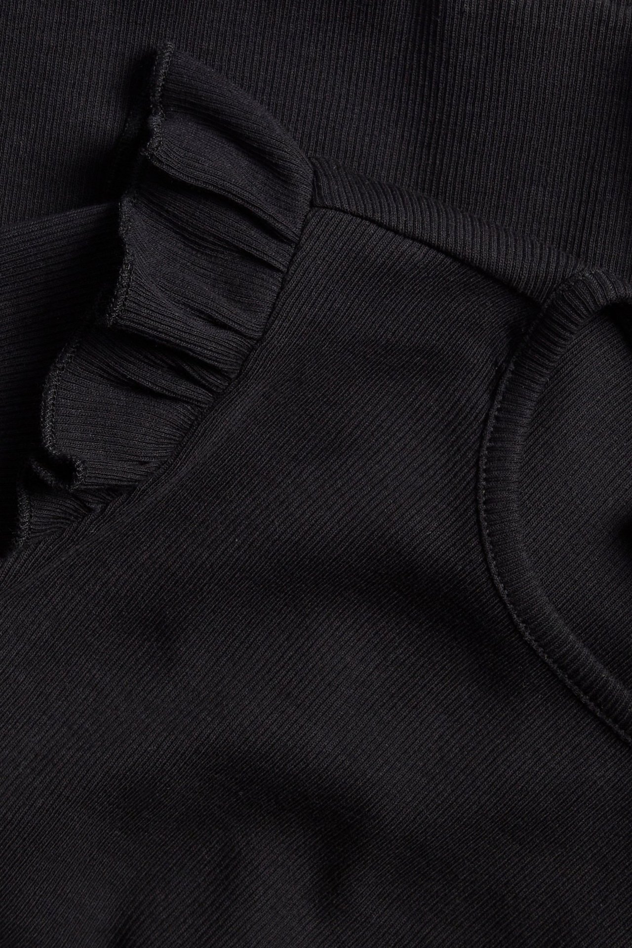Zbliżenie czarnej prążkowanej bluzki z długim rękawem z falbanką na ramieniu.