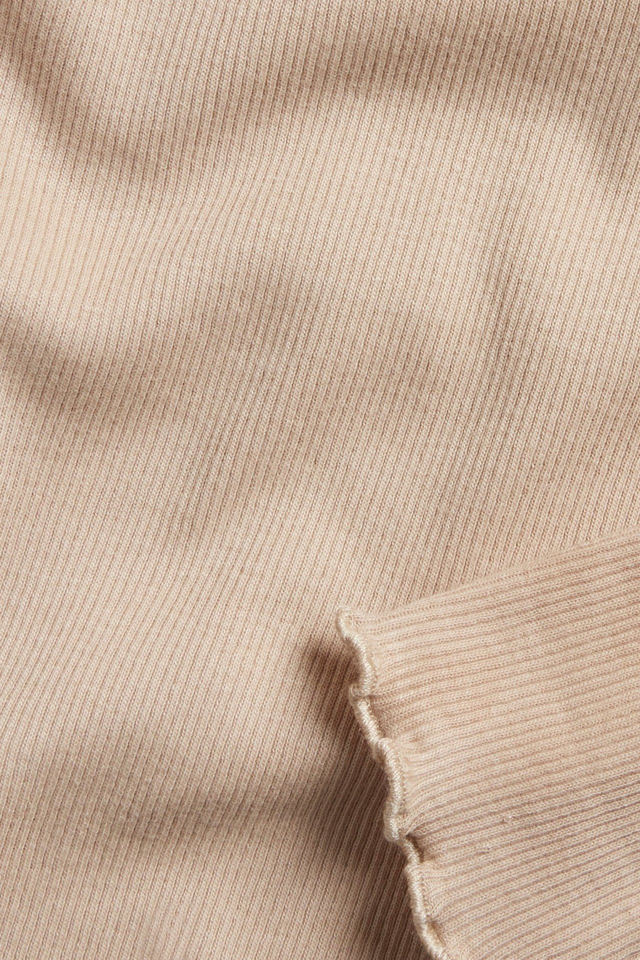 Zbliżenie beżowego prążkowanego topu z długim rękawem i falbanką.