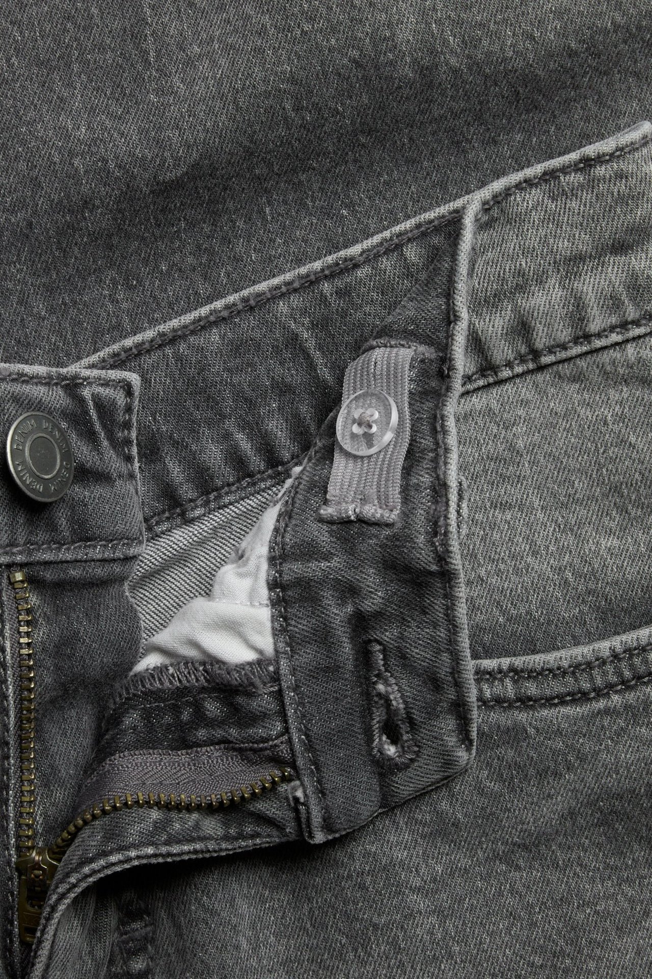 Lähikuva lasten harmaista slim fit -farkuista, joissa vetoketju, nappi ja säädettävä kuminauha vyötäröllä.