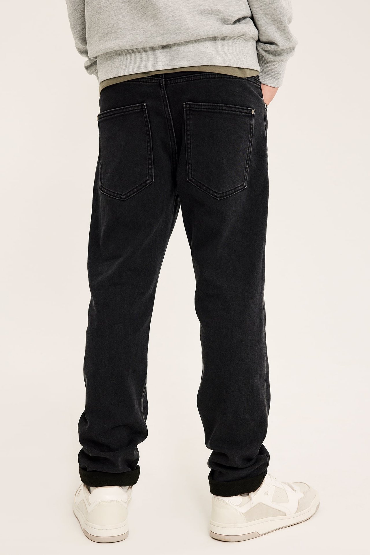 Bakfra en person i svarte oppbrettede rett-passform jeans, grå genser og hvite joggesko.
