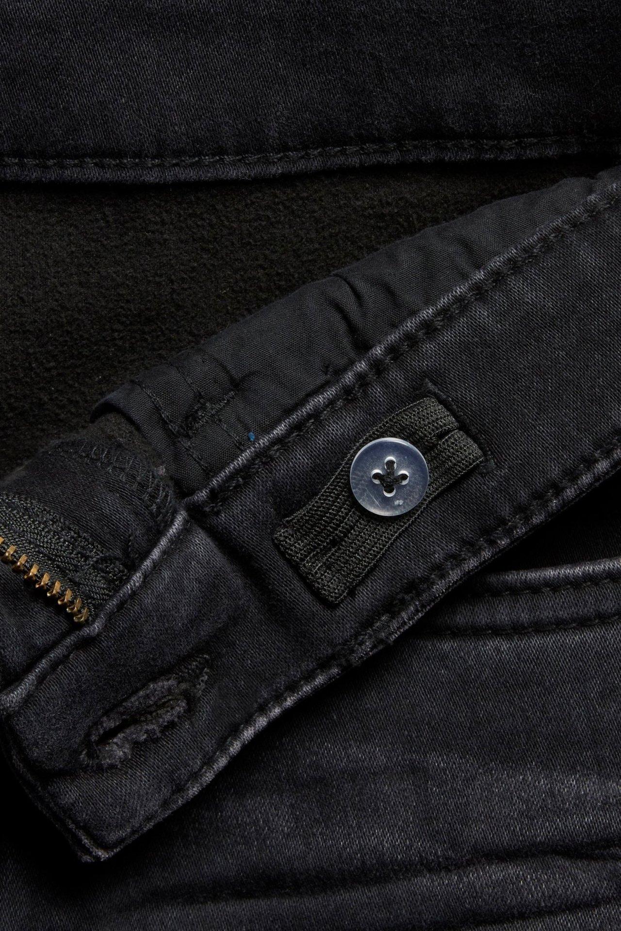 Zbliżenie na czarne dżinsy jogger denim z zamkiem, dziurką i regulowaną gumką z przezroczystym guzikiem.