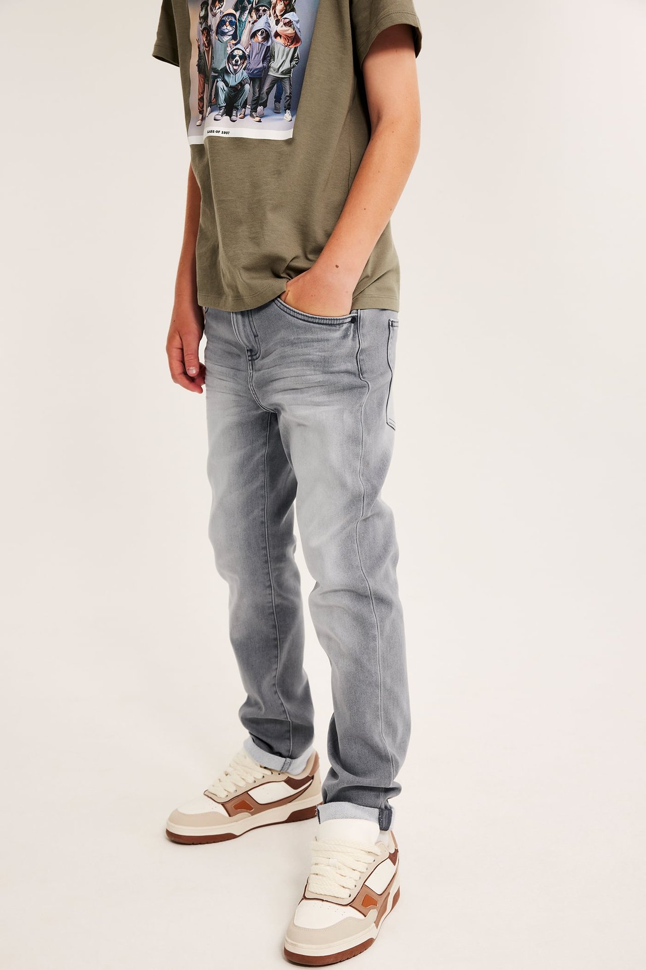 Barn, forfra: grå jeans, olivengrønn t-skjorte med trykk, flerfargede sneakers.