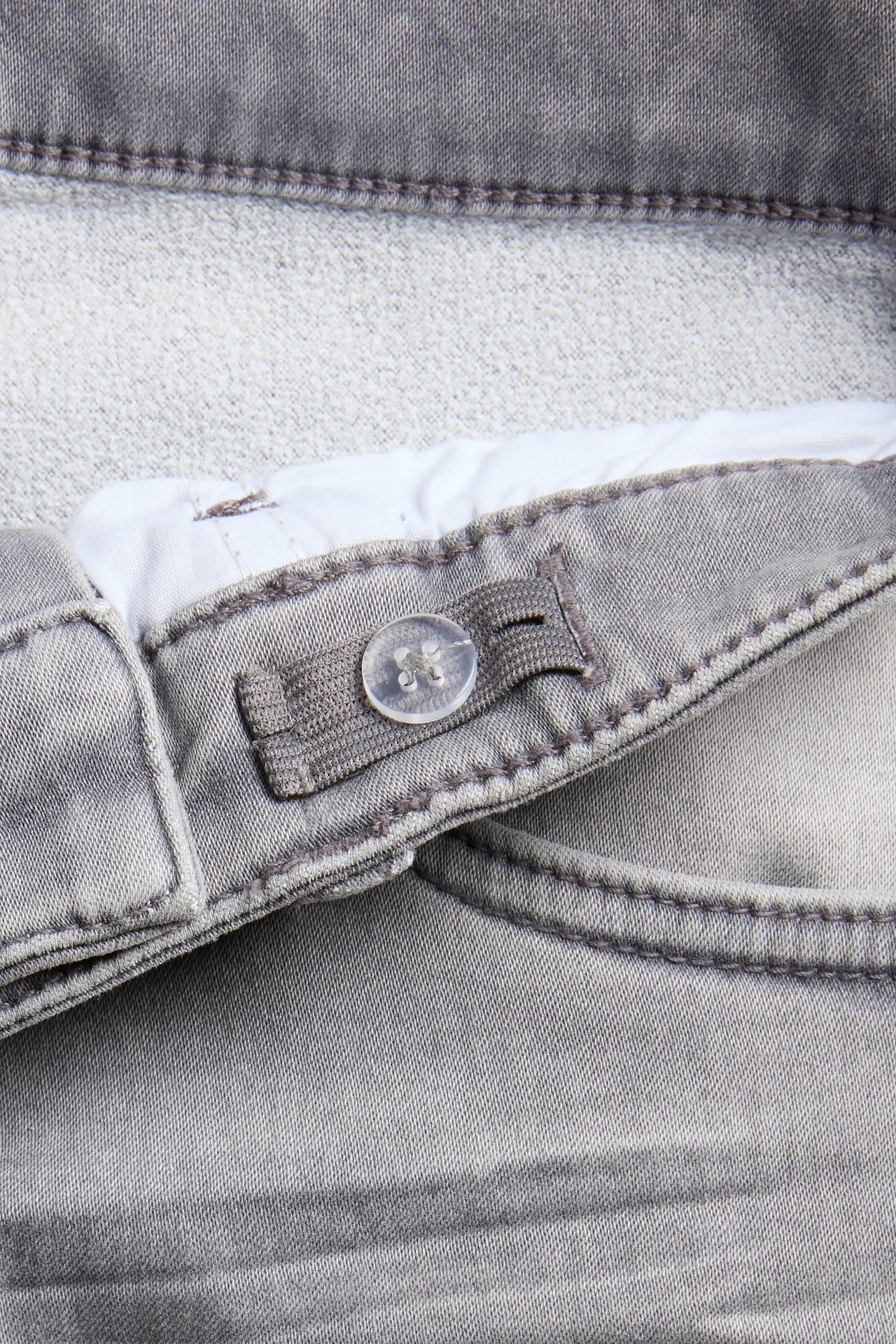 Zbliżenie szarych jeansów jogger denim relaxed, pokazujące regulowany pas z gumką i guzikiem.